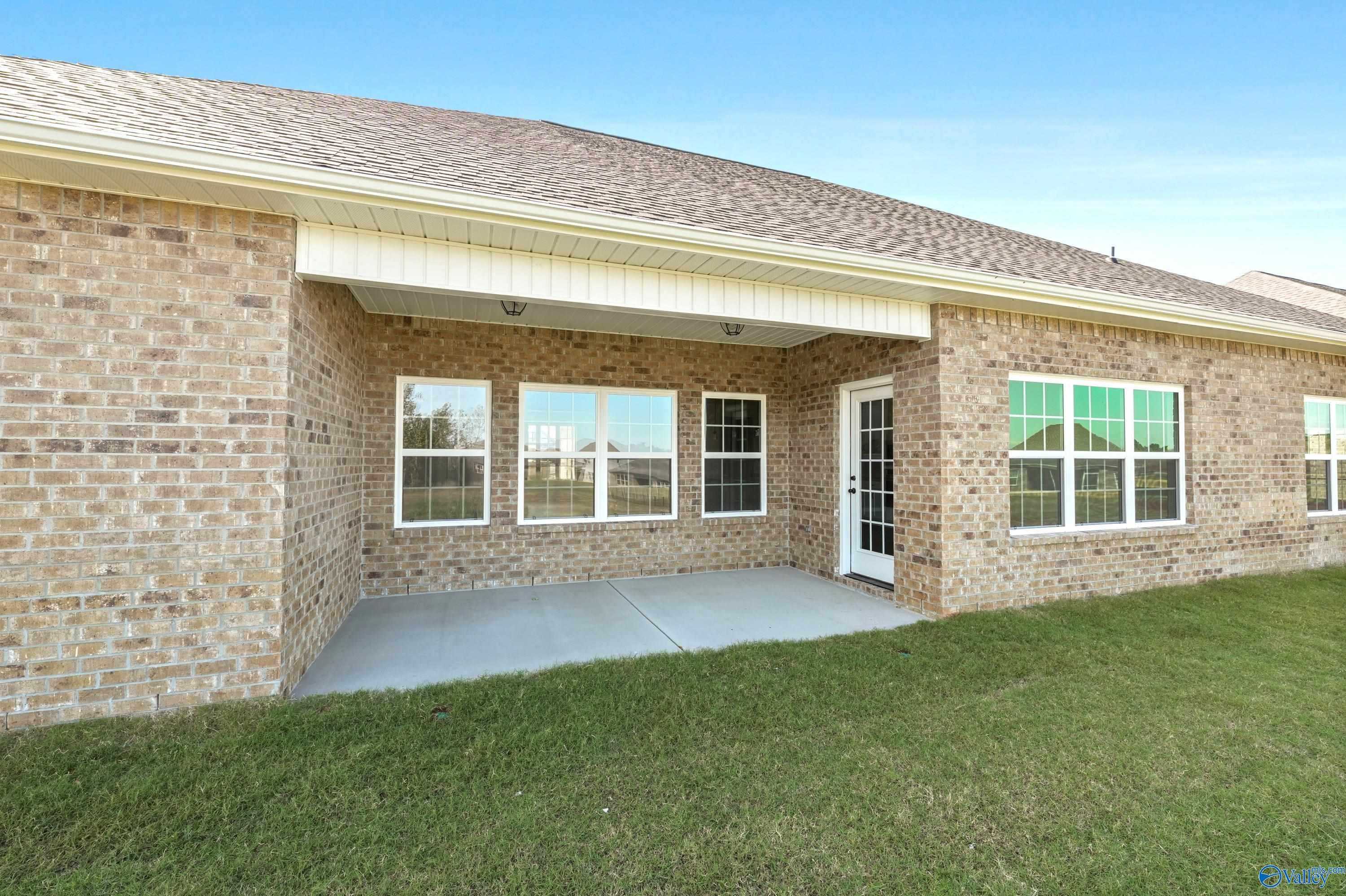 Brick exterior of The Finleigh 3-bedroom home featuring covered patio, large windows, and lush green lawn in Creekside, Harvest, Alabama