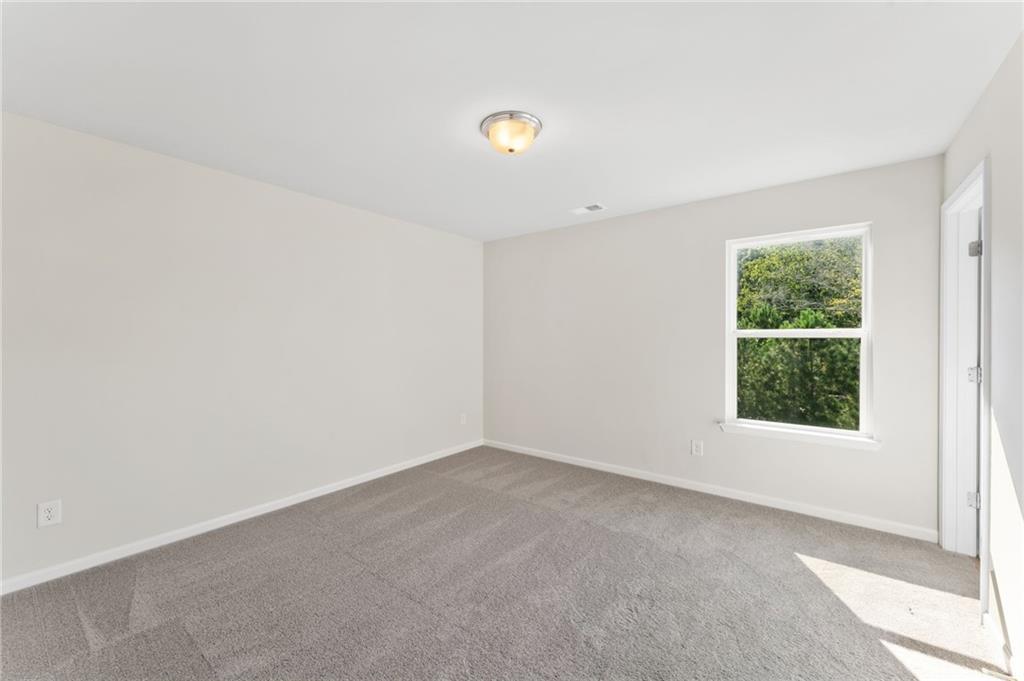 Bright secondary bedroom with beige walls, gray carpet, and large window to lush greenery in The Willow B, Davidson Homes, Riverwood, Dallas, Georgia