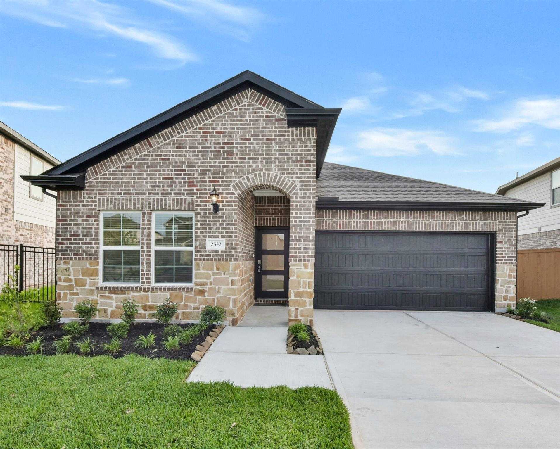 Modern brick single-story home with arched entry, 2-car garage, and lush landscaping in Sunterra, Katy, Texas - Davidson Homes The Laguna B