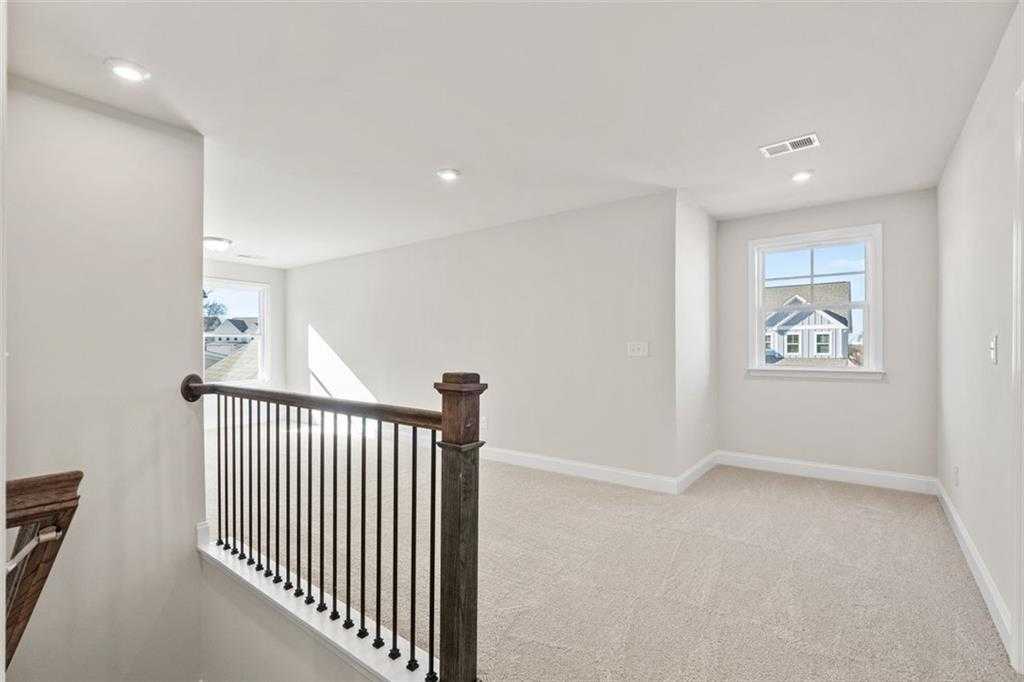 Spacious upstairs loft with wrought iron railing, carpeted floor, and large window overlooking neighborhood in Davidson Homes The Ash C, Wehunt Meadows, Hoschton, Georgia