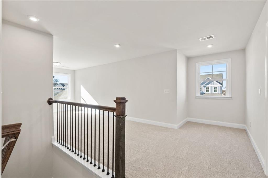 Spacious upstairs loft with wrought iron railing, carpeted floor, and large window overlooking neighborhood in Davidson Homes The Ash C, Wehunt Meadows, Hoschton, Georgia