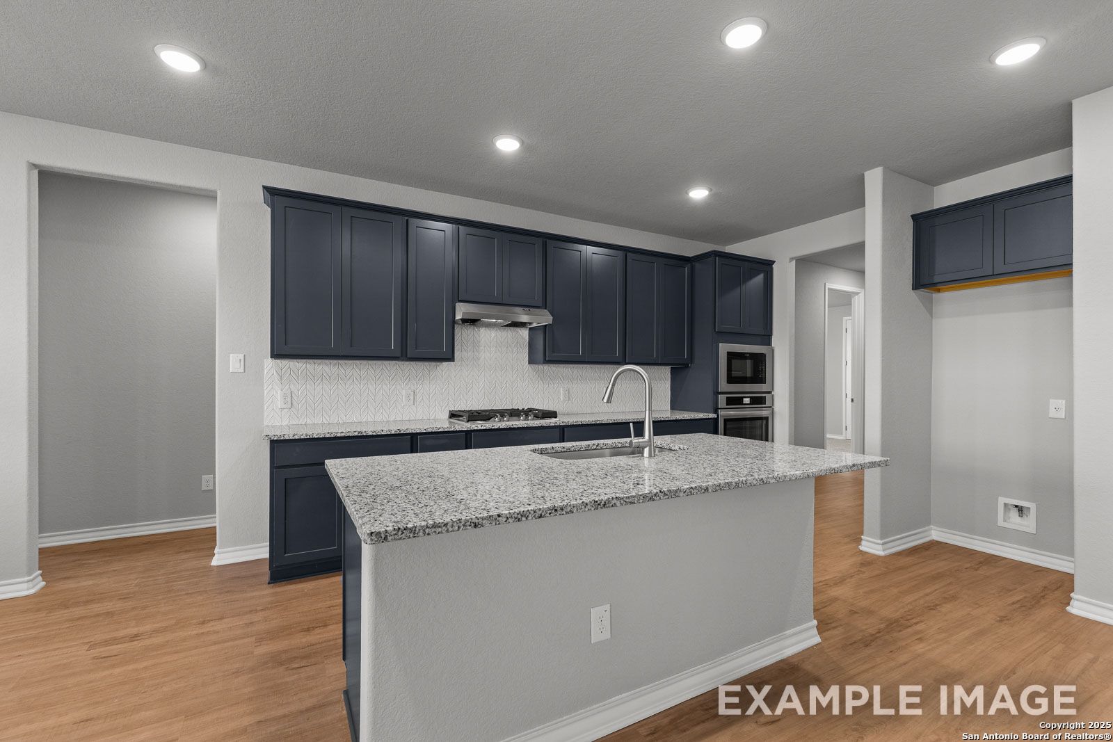 Modern kitchen in The Oxford H featuring dark blue cabinetry, granite island countertops, and chevron tile backsplash.