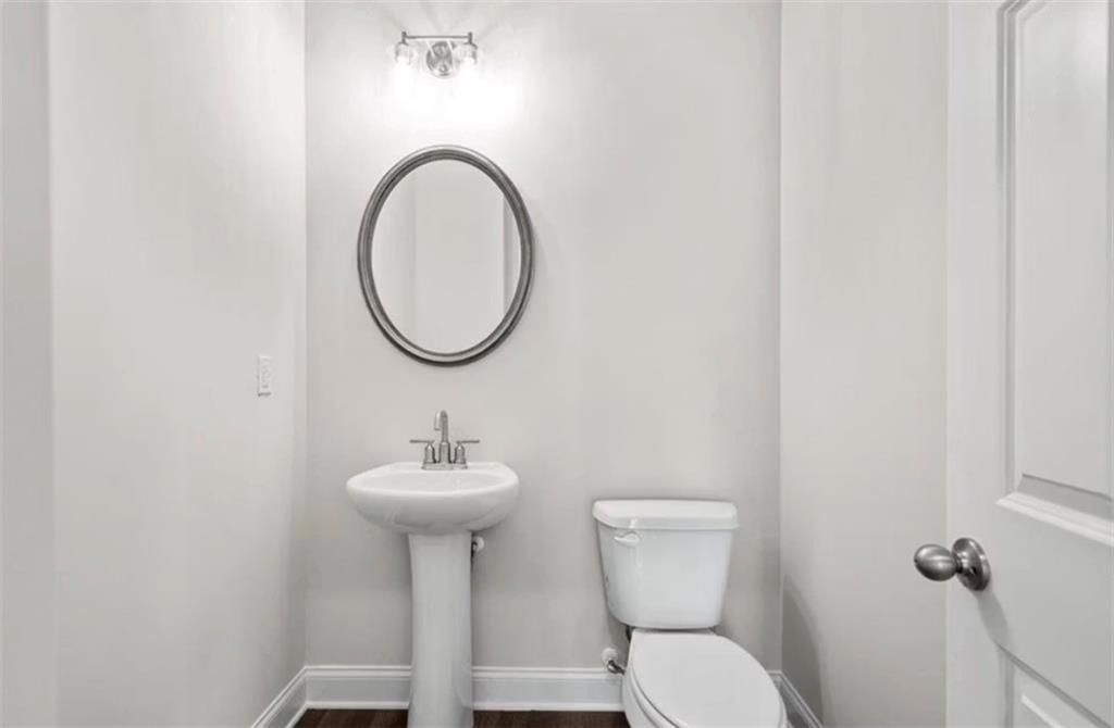 Modern half-bath with pedestal sink and round mirror in The Ash C floor plan at Wehunt Meadows, Hoschton, Georgia.