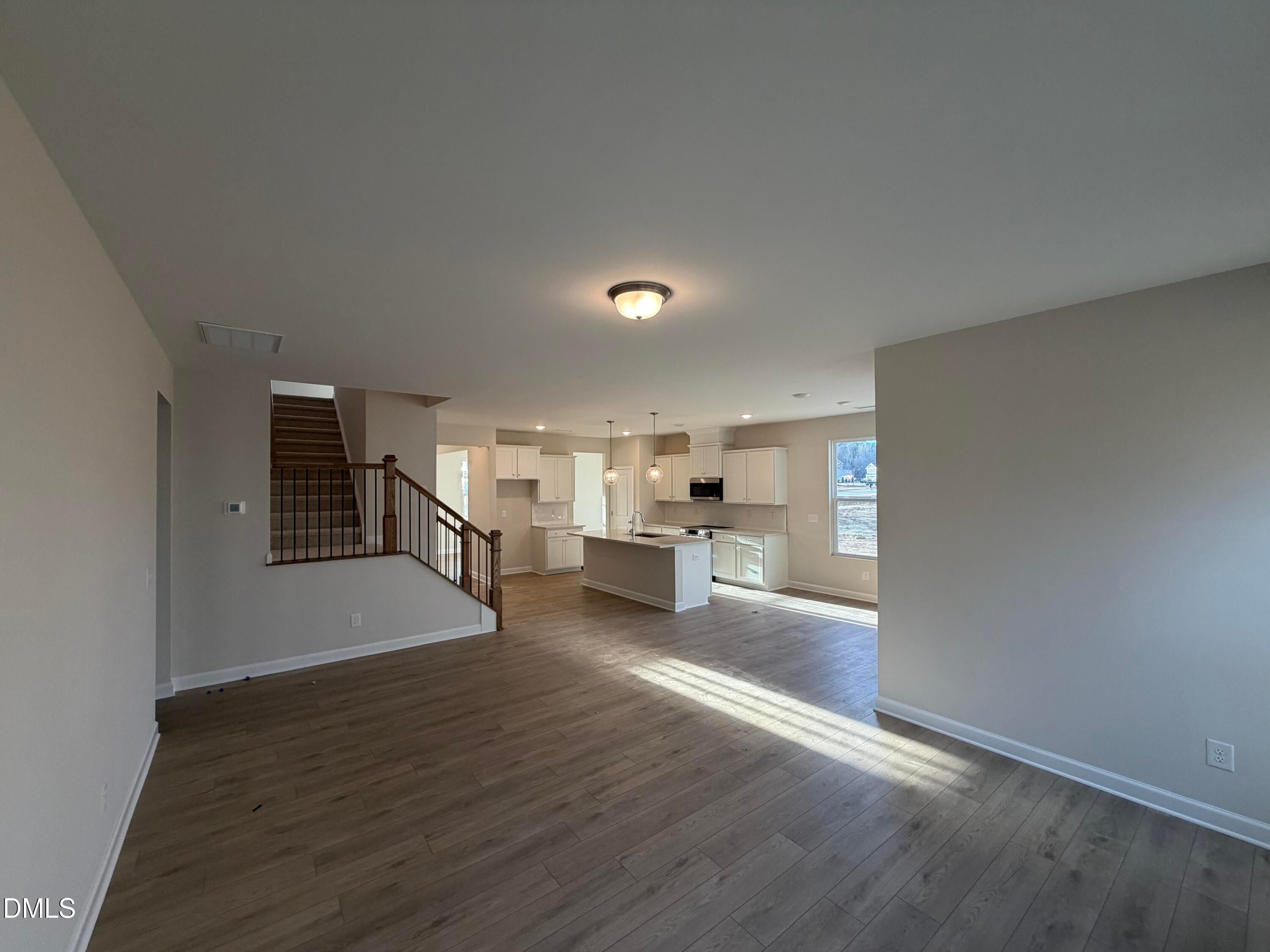 Open foyer with hardwood floors, wooden staircase, and white cabinet kitchen in Davidson Homes The Ash B, Lillington, NC