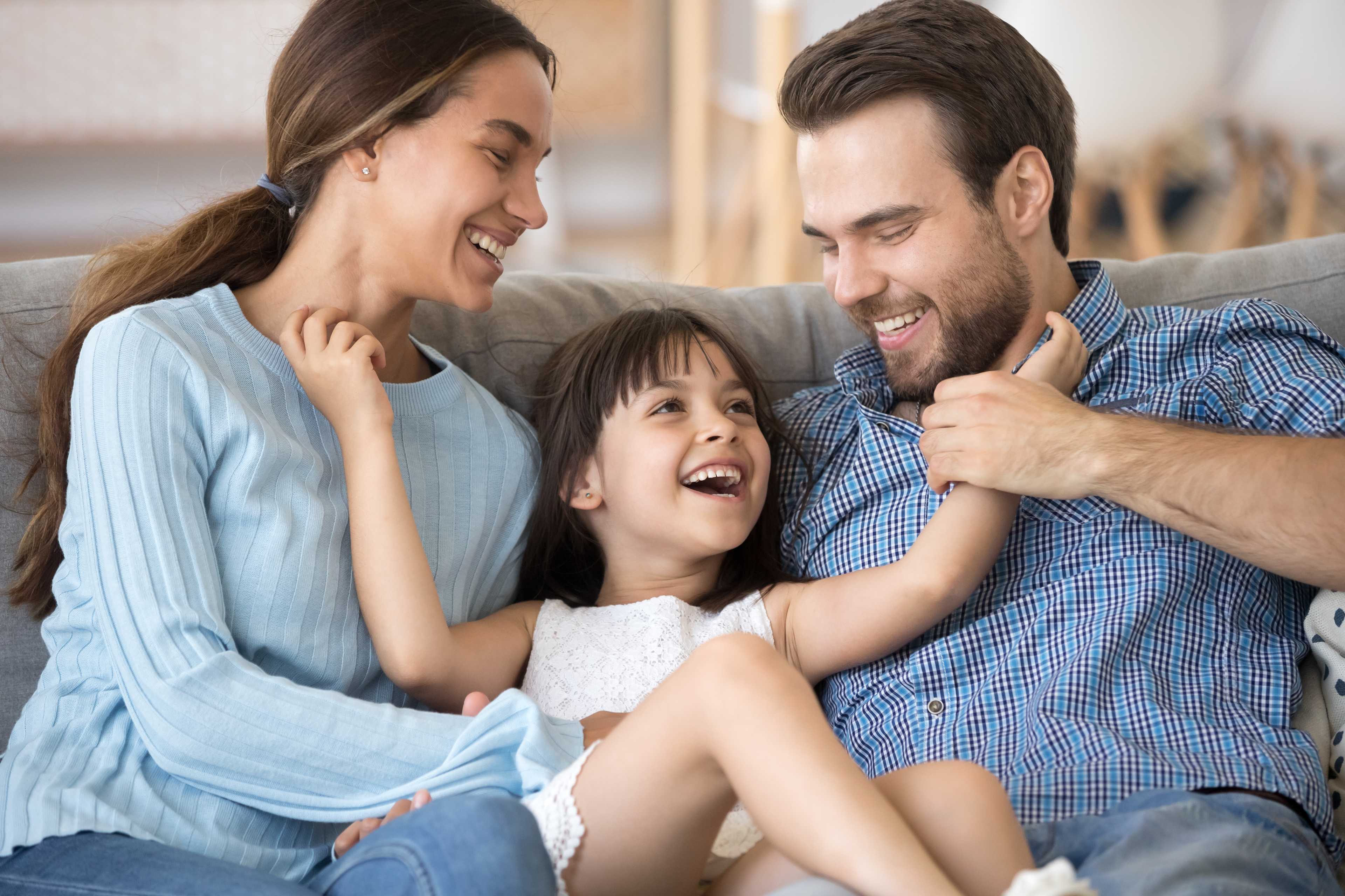 Joyful family laughing on gray sofa in modern living room at Lassiter Place, East Cobb, Georgia by Davidson Homes