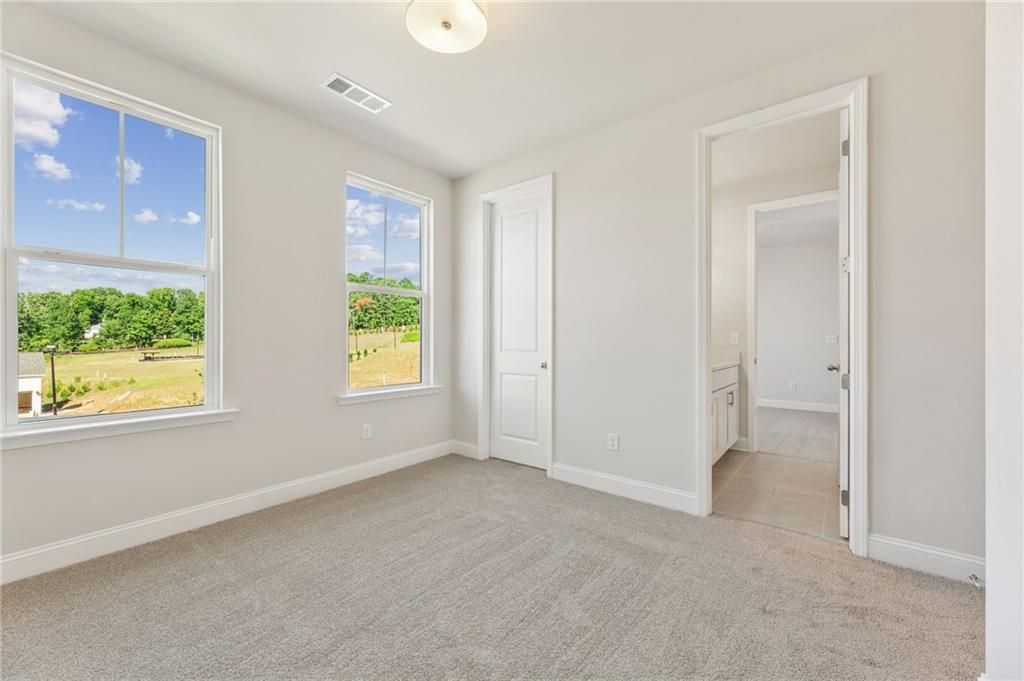 Bright bedroom with large windows overlooking green fields and trees in The Danbury E, Buford, Georgia