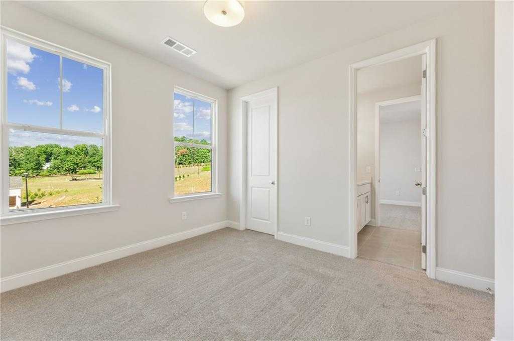 Bright bedroom with large windows showcasing green fields and blue sky views in Davidson Homes The Danbury E, Buford, Georgia