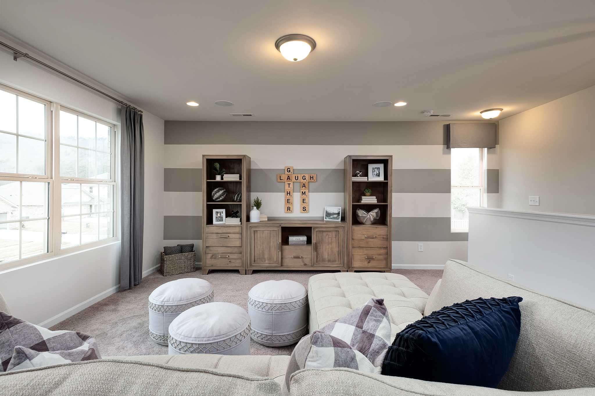 Cozy family room at The Reserve at Overton in Hampton Cove Alabama with neutral striped walls, wood media console, and plush sectional sofa