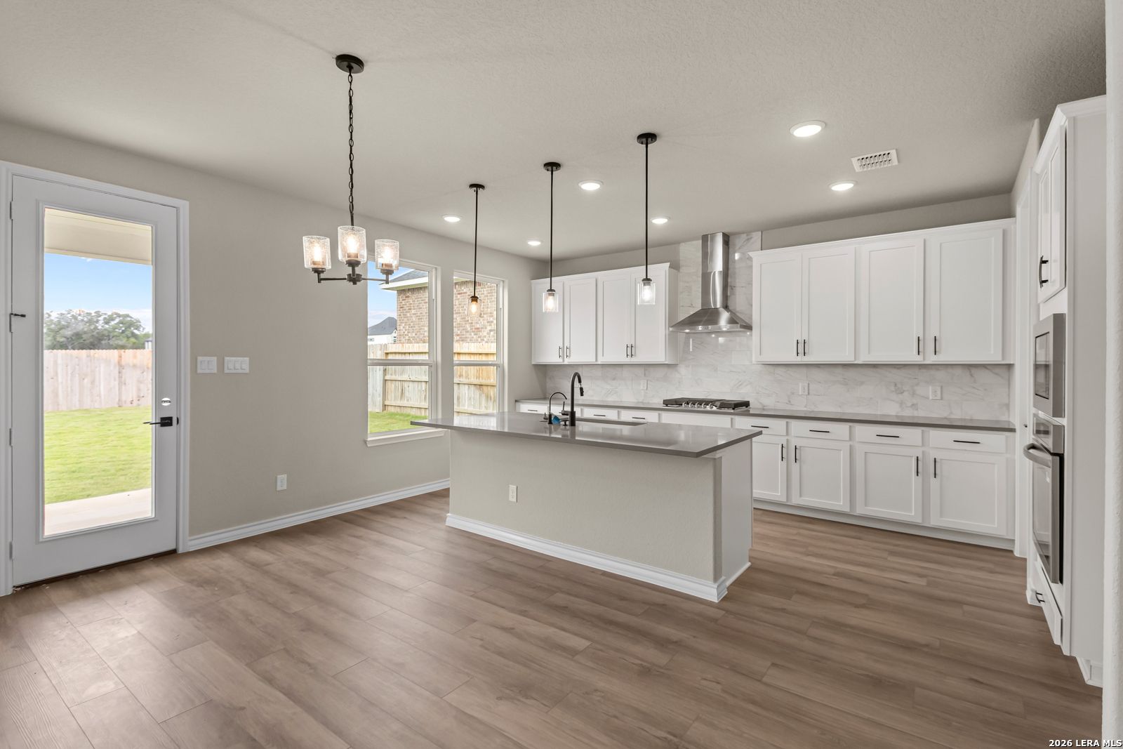 Modern open kitchen with white cabinets, large island, and stainless appliances in The Danbury H home, Castroville, Texas.