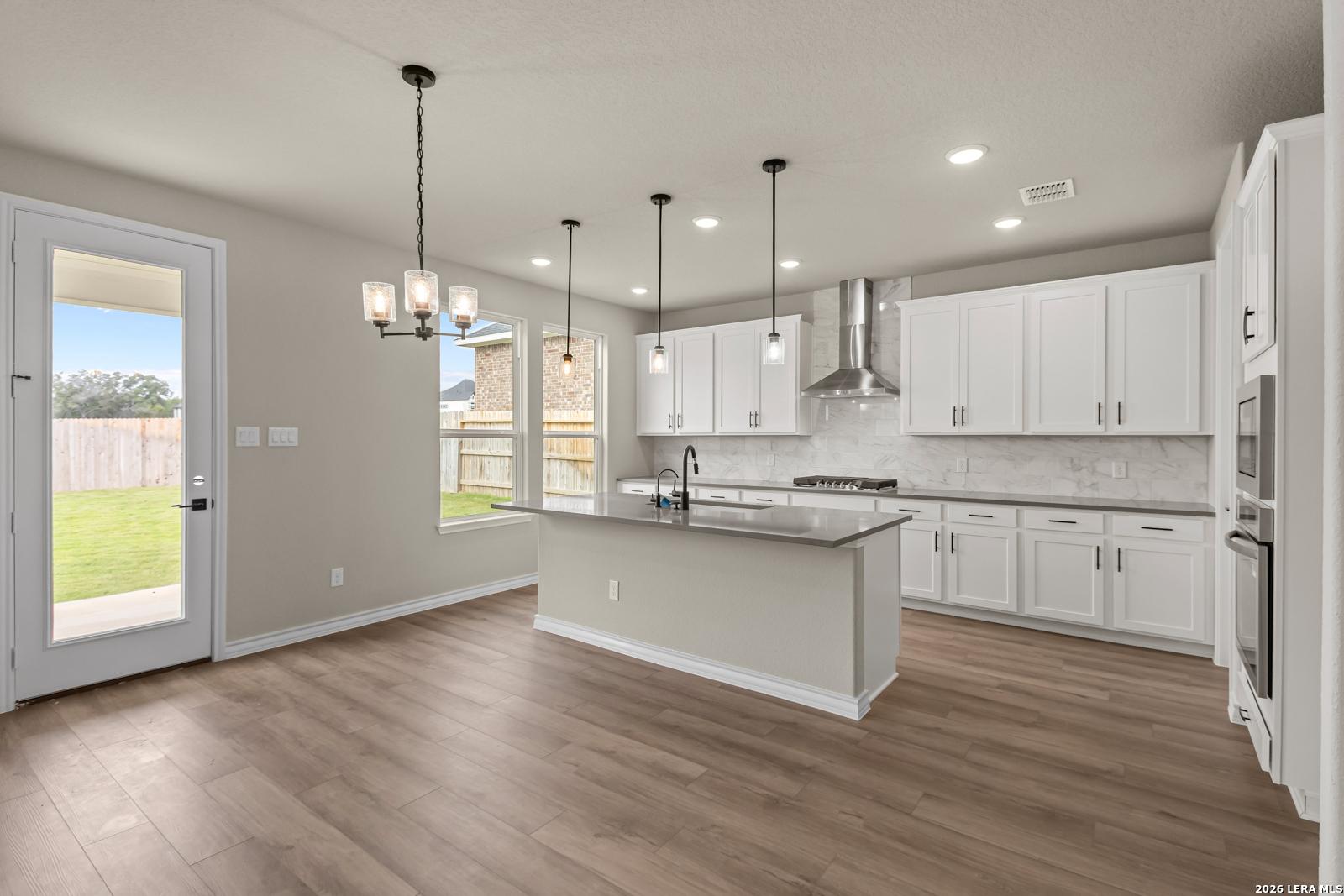 Modern open kitchen with white cabinets, large island, and stainless appliances in The Danbury H home, Castroville, Texas.