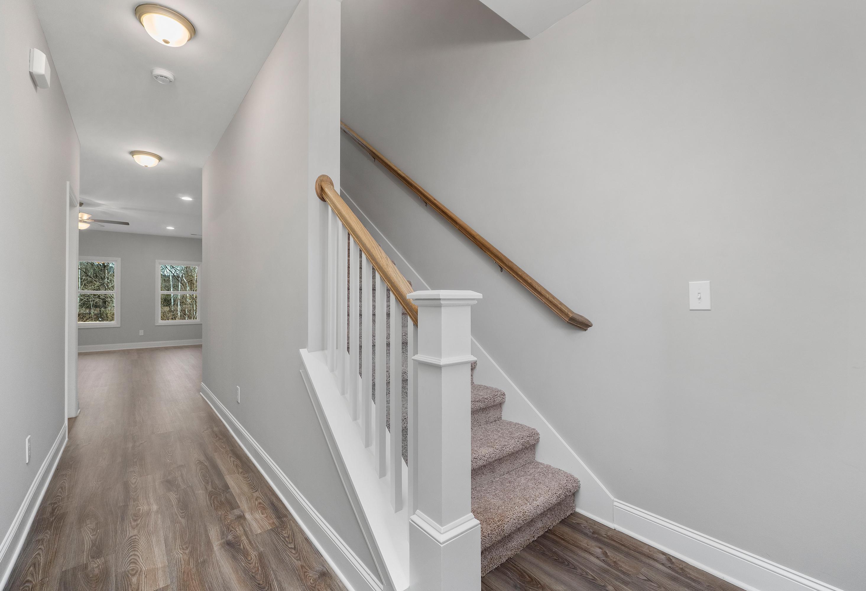 Bright hallway with gray walls, hardwood floors, and white-railed carpeted staircase in The Aiken 2-story home by Davidson Homes