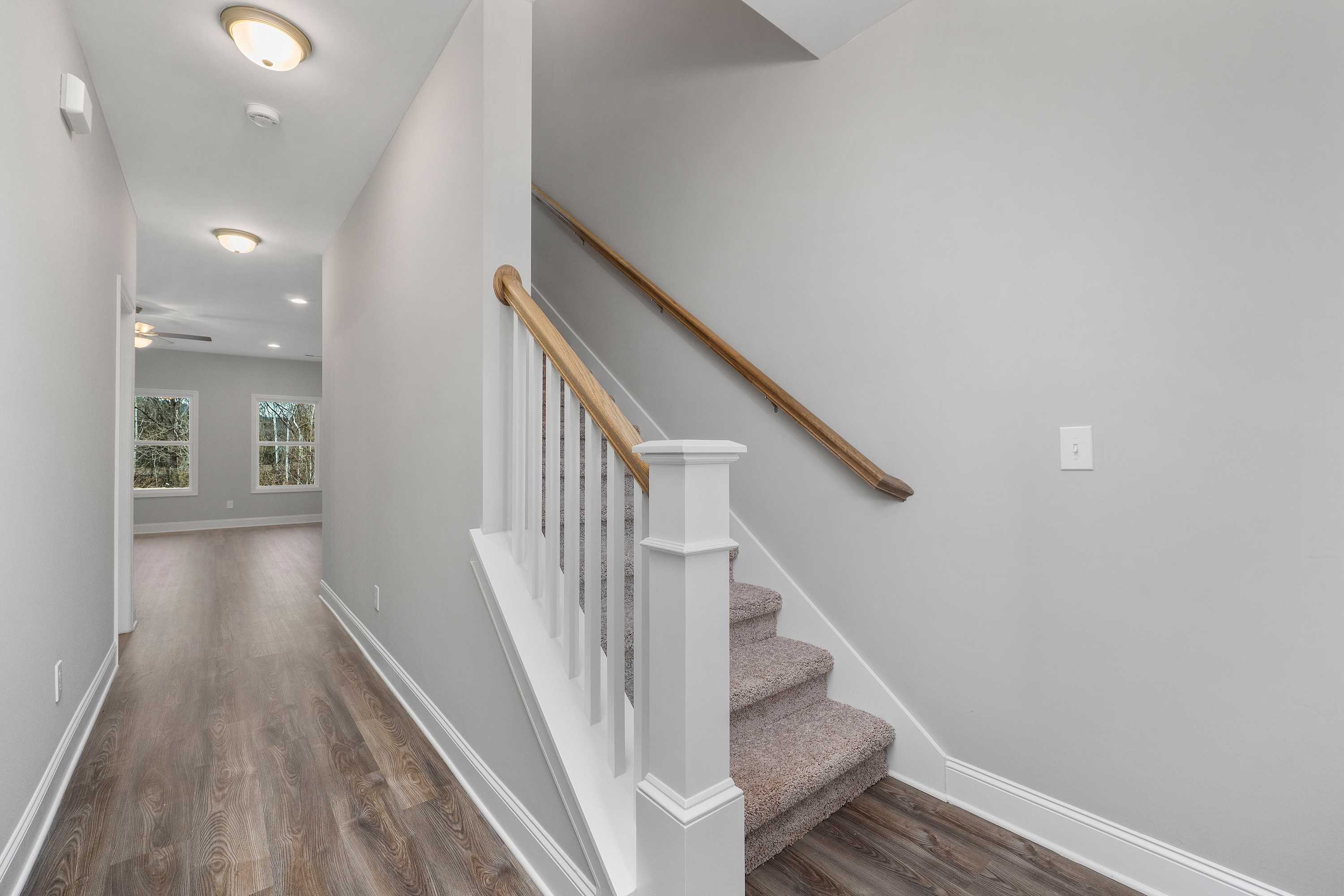 Bright hallway with gray walls, hardwood floors, and white-railed carpeted staircase in The Aiken 2-story home by Davidson Homes