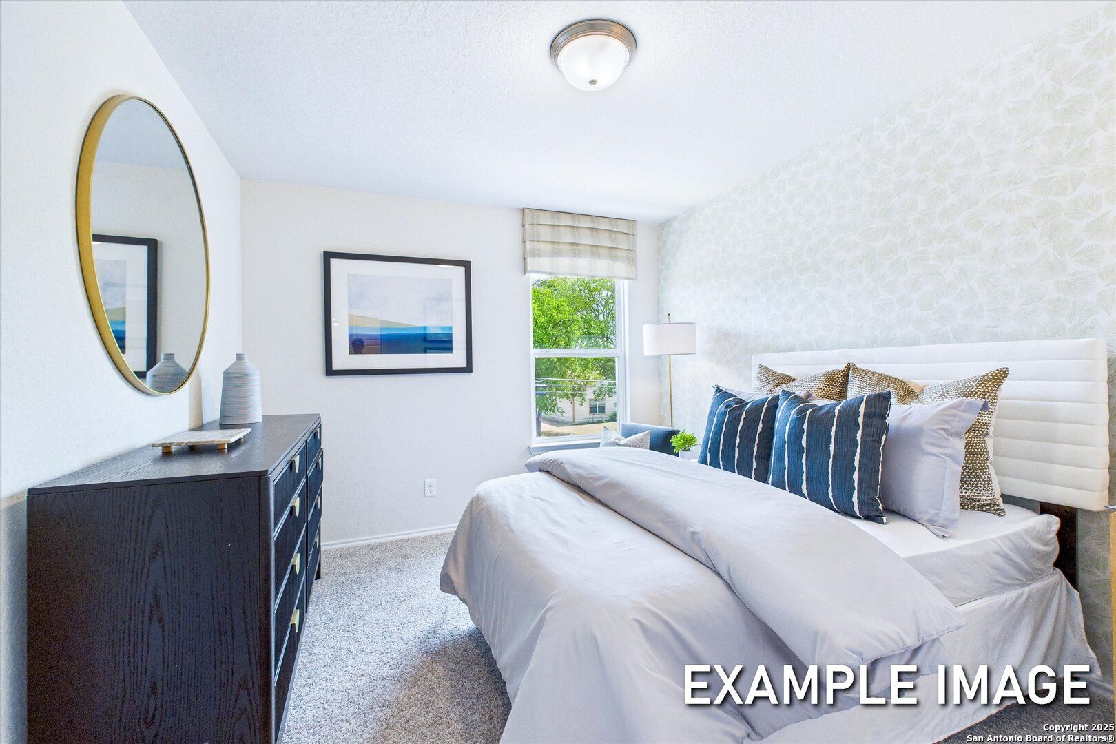 Cozy secondary bedroom with king bed, blue pillows, black dresser, gold mirror, and window in The Gillian B, San Antonio
