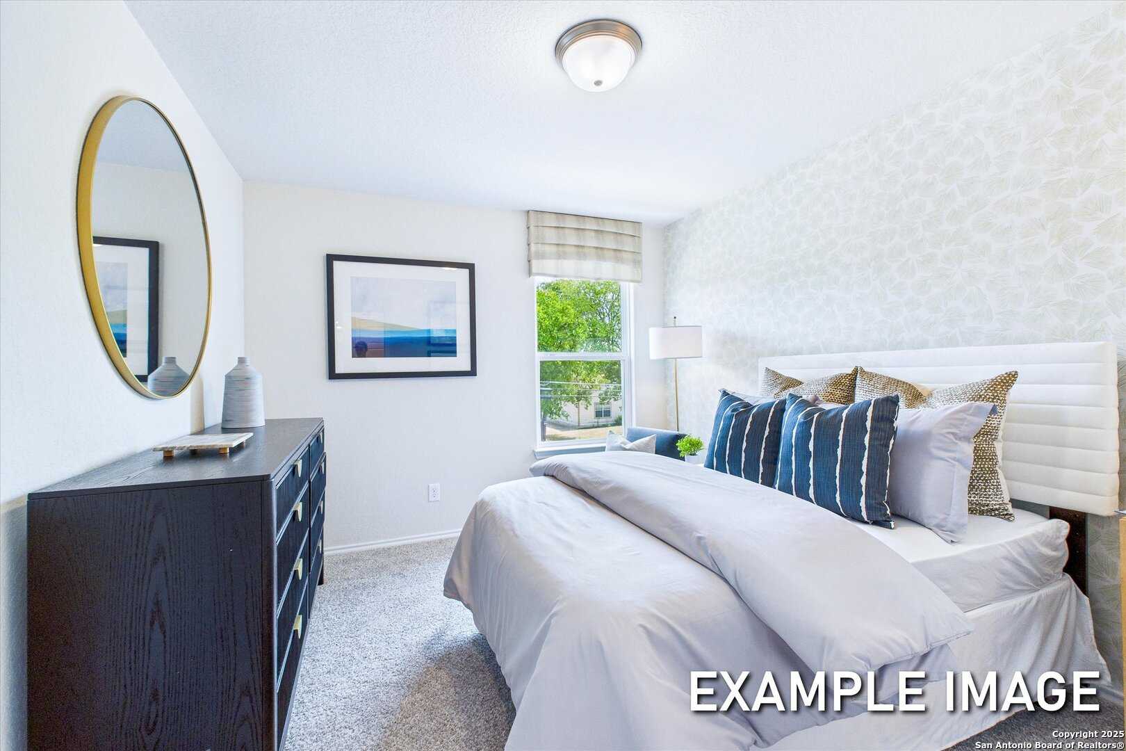 Cozy secondary bedroom with queen bed, gray linens, blue pillows, round mirror, and dresser in Davidson Homes The Gillian C, San Antonio