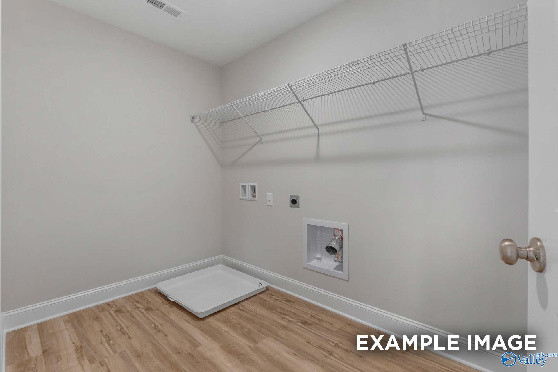 Functional laundry room with wire shelving, utility sink, washer/dryer hookups on hardwood floors in Davidson Homes The Shelby C, Meridianville, Alabama