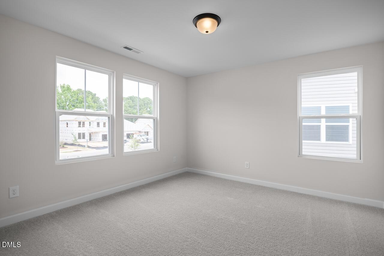 Bright, carpeted bedroom with neutral walls and multiple windows in The Willow B floor plan at Woodland Crossing, Zebulon.