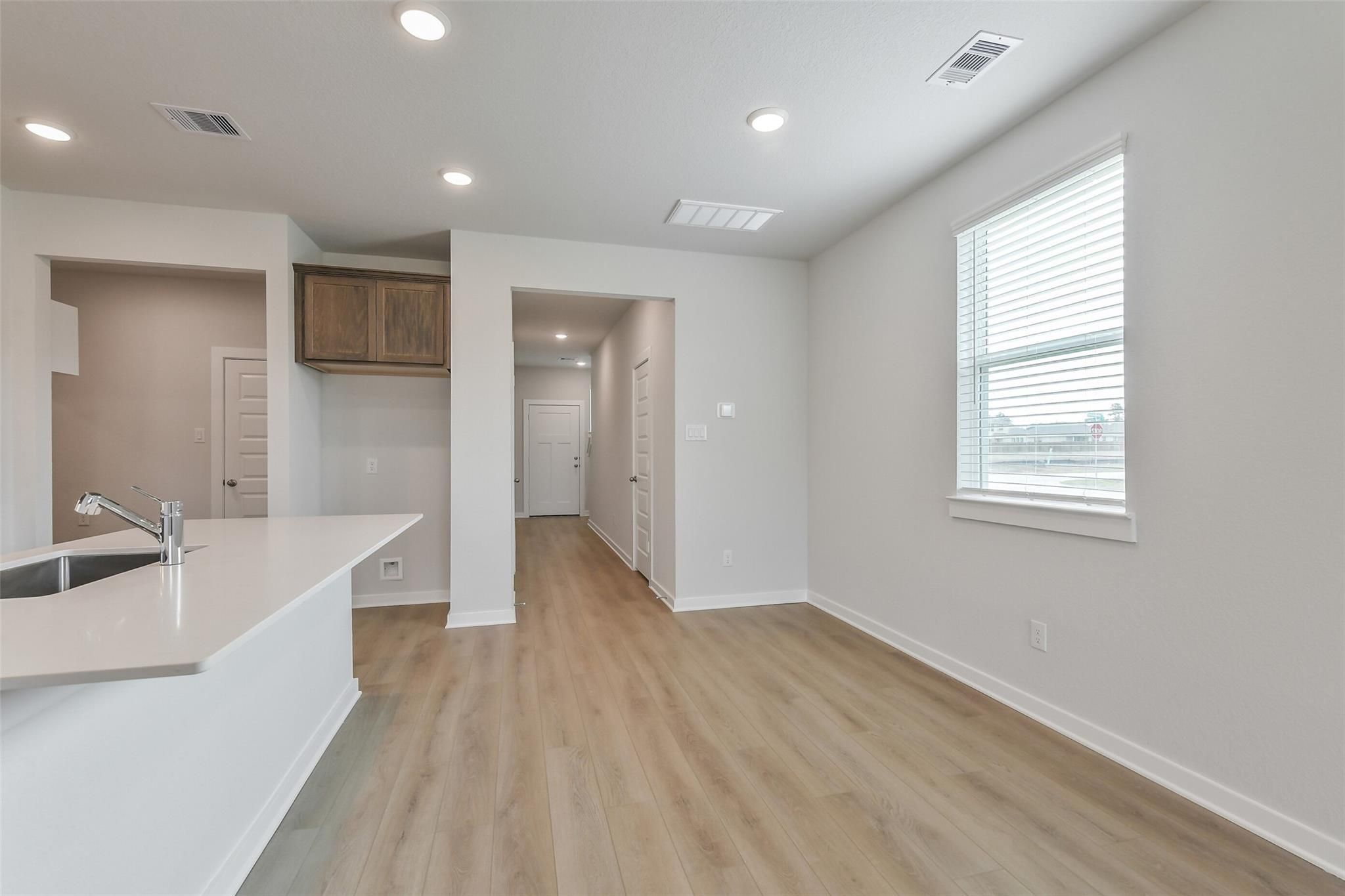 Modern open-concept kitchen with white island sink and wood cabinets in Davidson Homes The Brazos E, Cleveland Texas