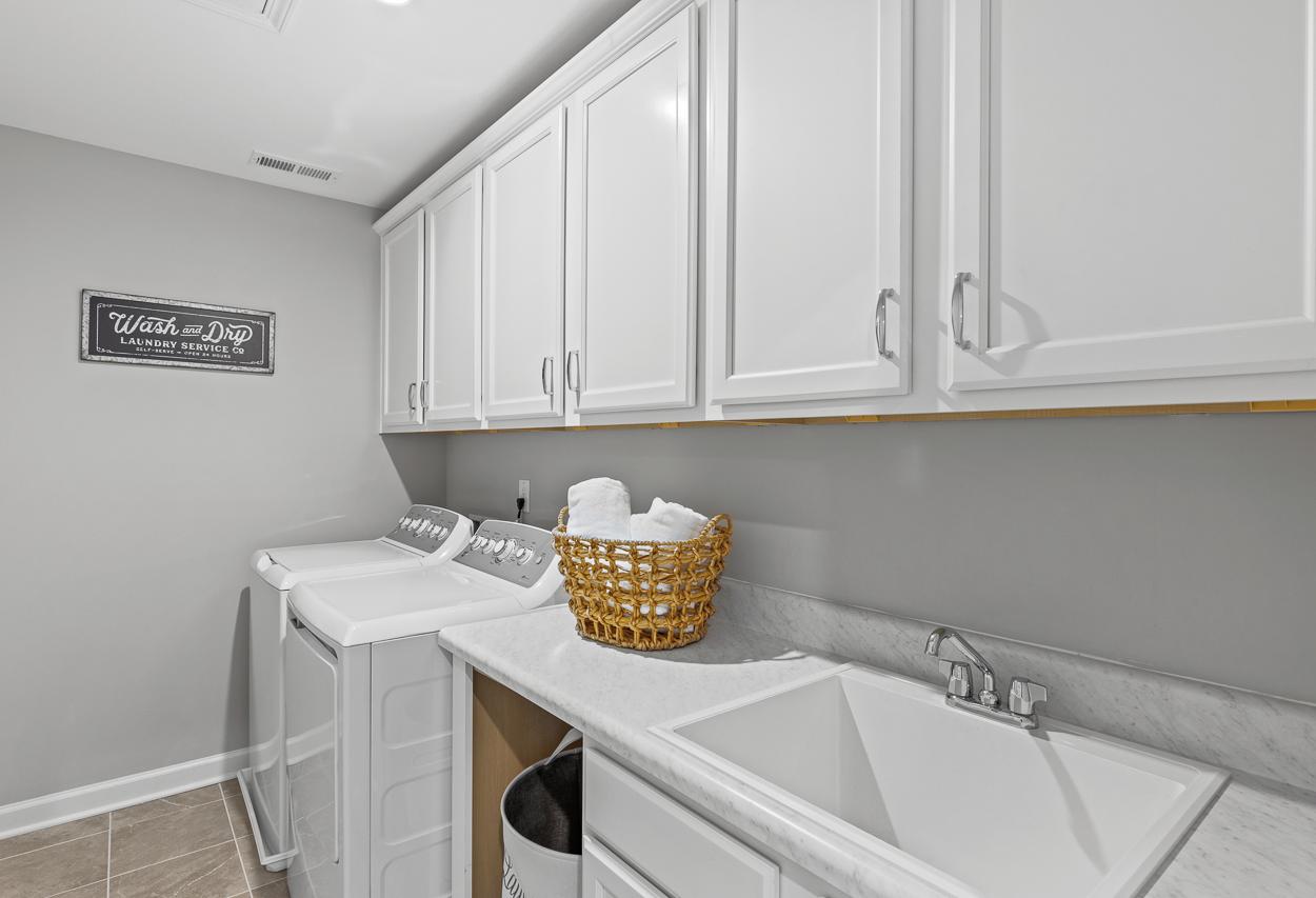 Laundry room in The Hemlock model featuring white cabinets, marble-look countertops, deep utility sink, and washer/dryer.