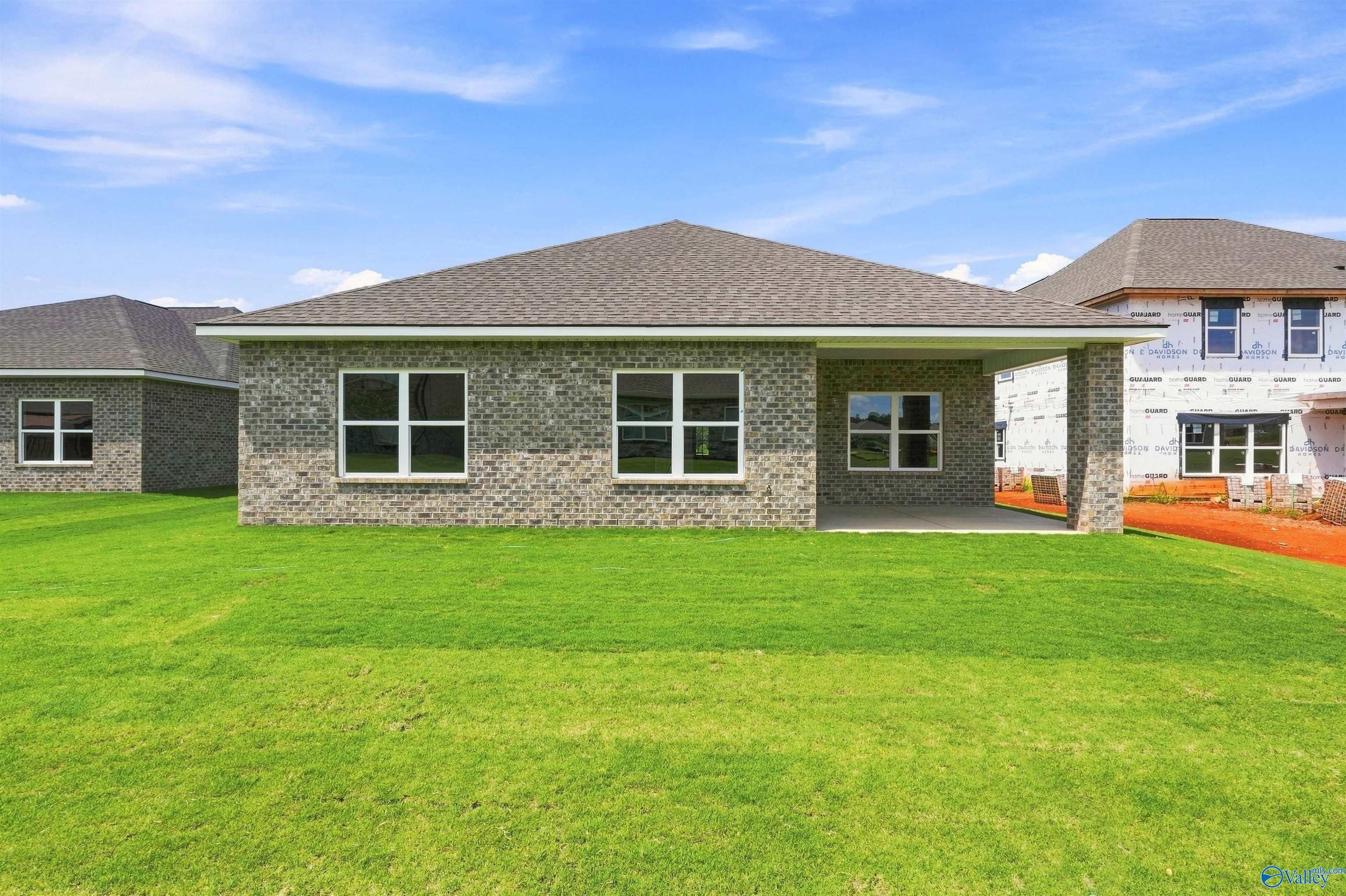 Rear exterior of gray brick Davidson Homes Everett B house with covered patio and lush backyard in Wood Trail, Toney, Alabama