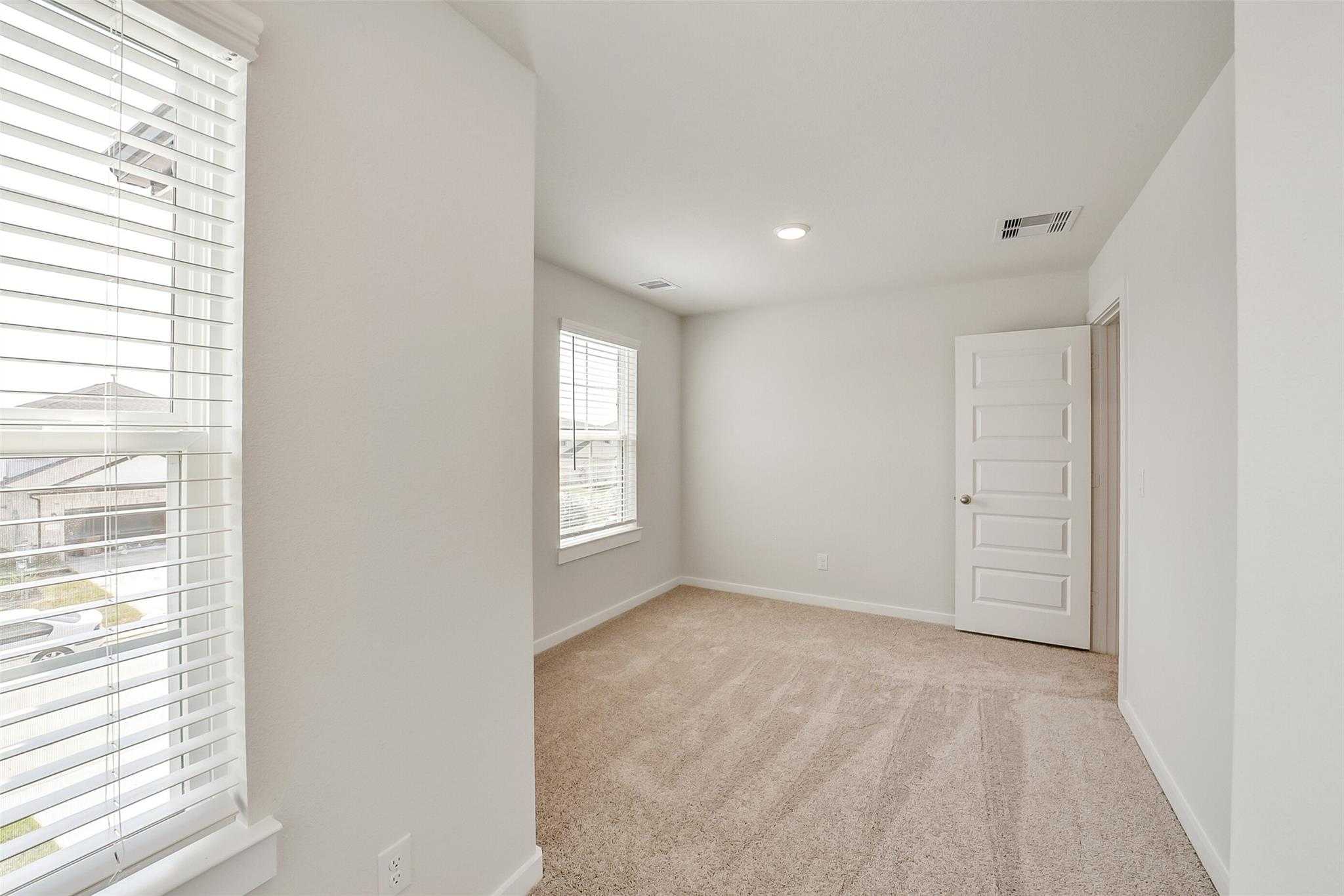 Bright secondary bedroom with beige carpet, white walls, and double windows in Davidson Homes The Blanco E, Magnolia, Texas