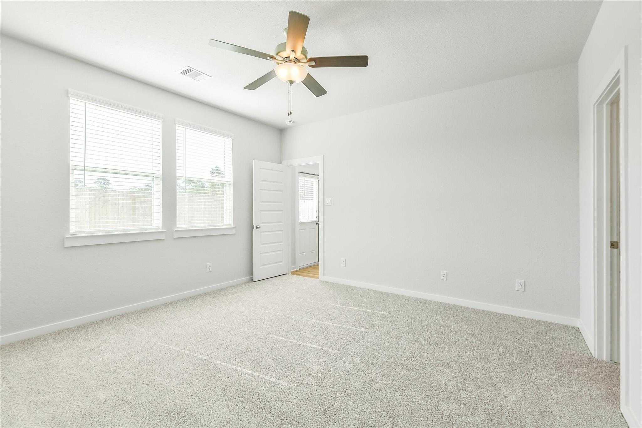 Spacious empty bedroom with beige carpet, ceiling fan, and large window blinds in The San Marcos E by Davidson Homes, Cleveland Texas