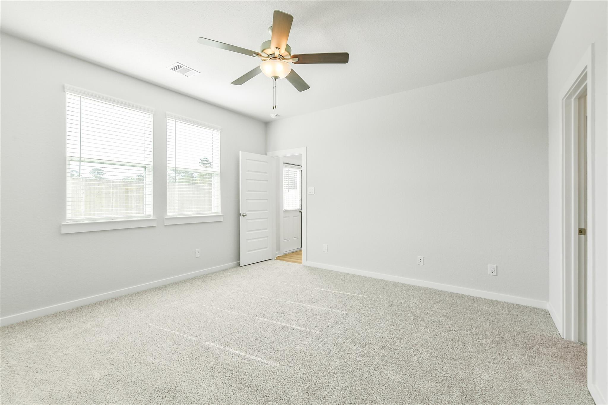 Spacious empty bedroom with beige carpet, ceiling fan, and large window blinds in The San Marcos E by Davidson Homes, Cleveland Texas