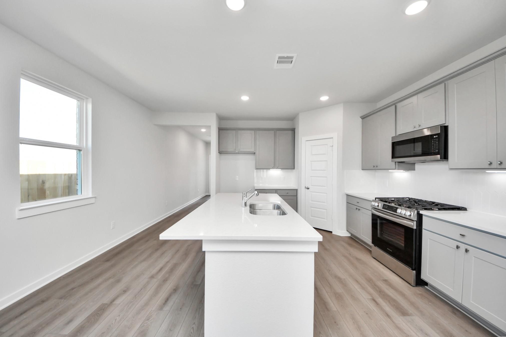 Modern kitchen with white quartz island, gray cabinets, and stainless steel appliances in The Riviera A, Emberly, Beasley.