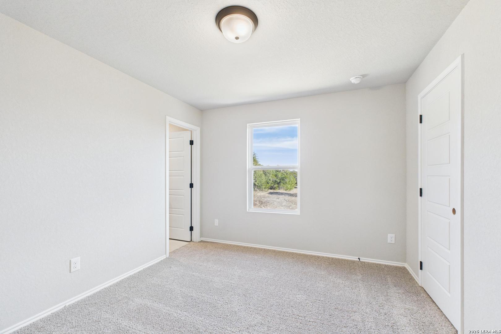 Bright secondary bedroom with beige carpet, ceiling fan light, large window, and double doors in Davidson Homes The Douglas E, San Antonio