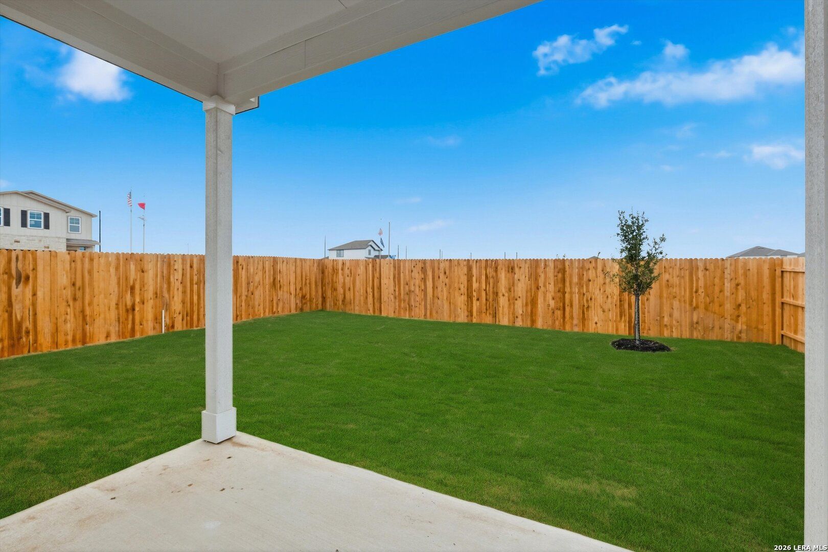 Covered patio overlooking private green backyard with young tree and wooden fence in Davidson Homes The Frio B, Agave, San Antonio