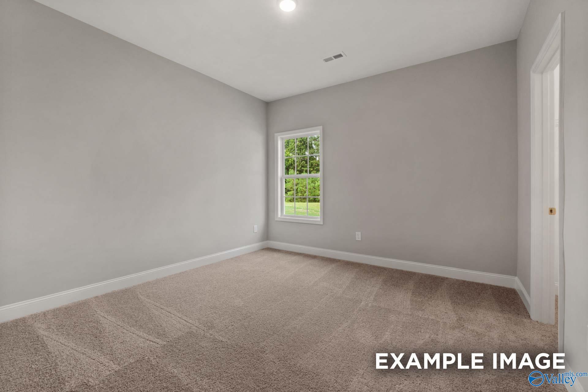 Spacious empty bedroom with light gray walls, beige carpet, large window overlooking greenery in Davidson Homes The Montgomery B, Toney, Alabama