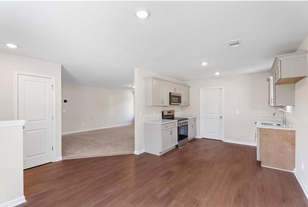 Open-concept kitchen with white cabinets, stainless steel appliances, and hardwood floors in Davidson Homes The Washington, Phenix City, Alabama
