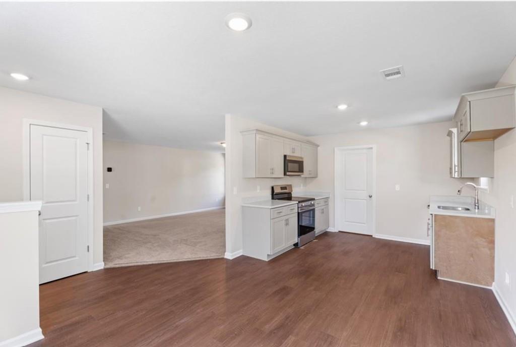 Open-concept kitchen with white cabinets, stainless steel appliances, and hardwood floors in Davidson Homes The Washington, Phenix City, Alabama