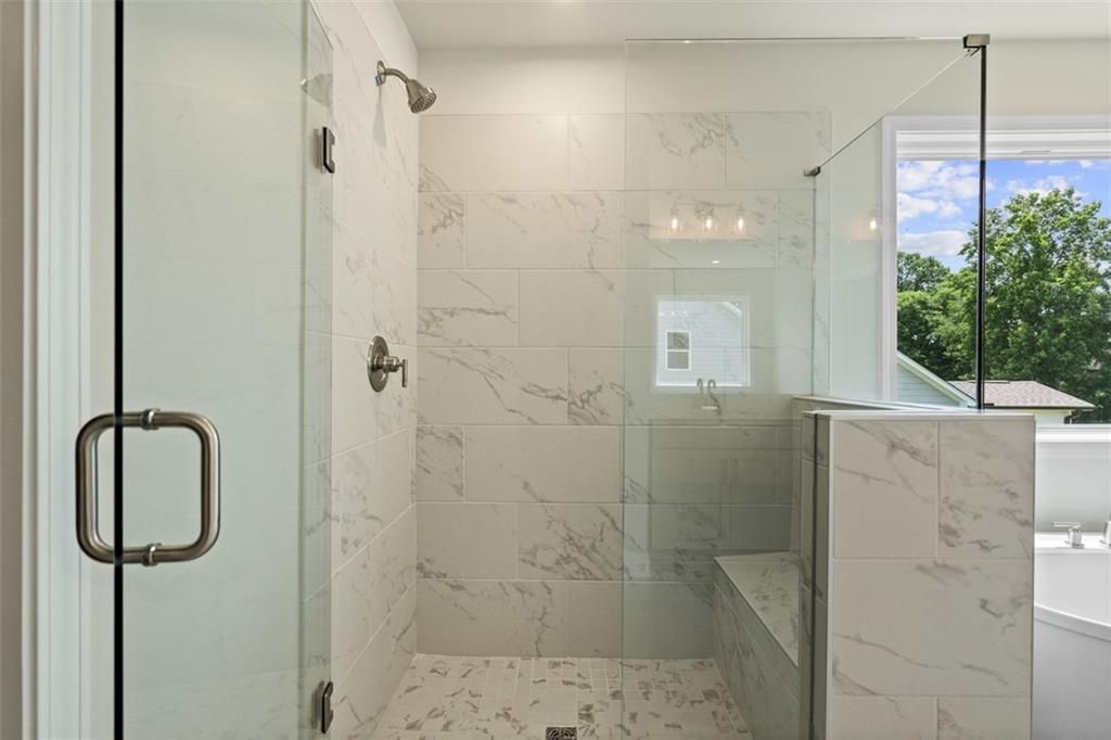 Luxurious master bath with frameless glass shower, marble tile walls, bench seat, and soaking tub in Davidson Homes Hickory B at Wehunt Meadows, Hoschton