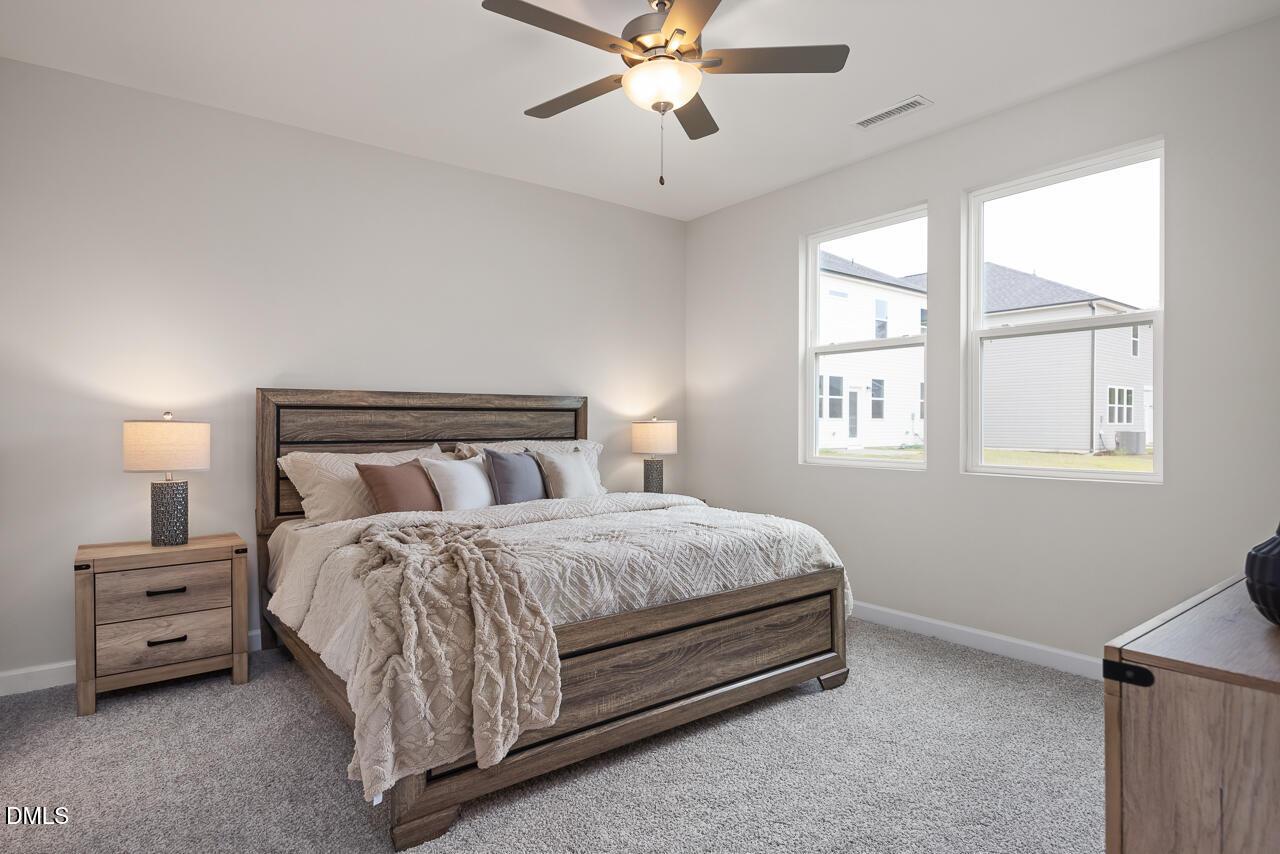 Cozy master bedroom with wooden bed, plush pillows, ceiling fan, and large windows in Davidson Homes The Carter C, Lillington, NC