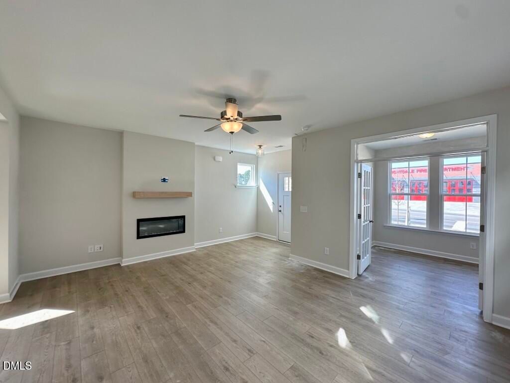 Cozy open living room with gas fireplace, ceiling fan, and light hardwood floors in The Burke 3-bedroom home, Knightdale, NC