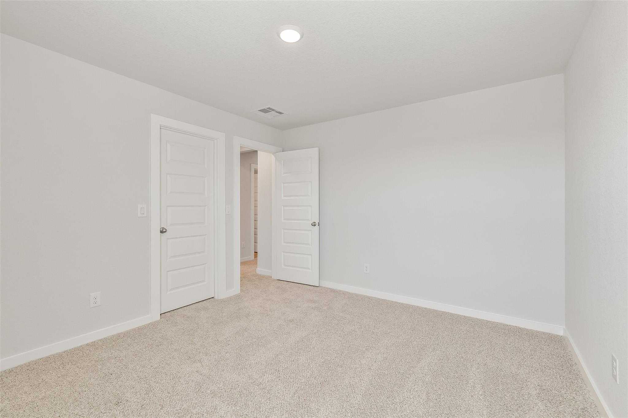Spacious secondary bedroom with neutral walls, beige carpet, and double doors in Davidson Homes The Rio Grande H, Magnolia, Texas