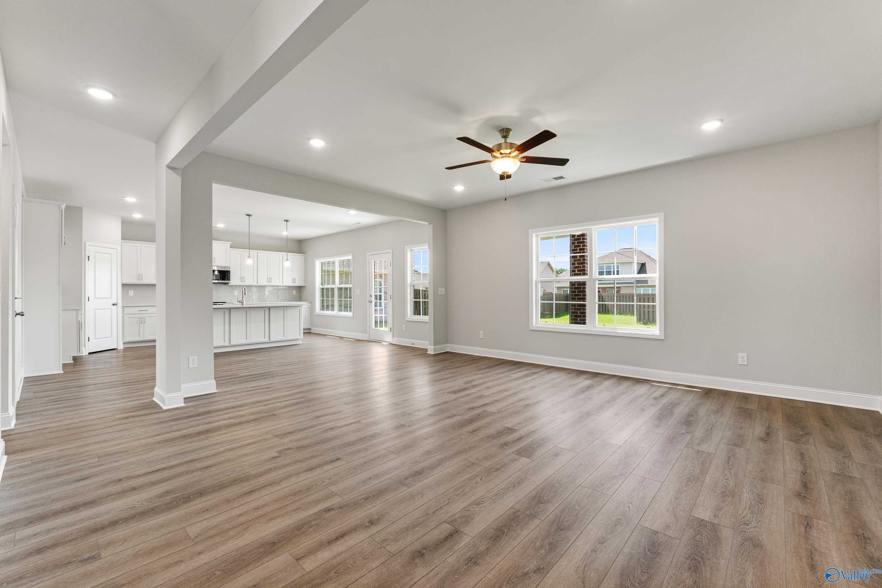 Open-concept living area with hardwood floors, ceiling fan, and large windows overlooking yard in Davidson Homes The Madison A, Toney, AL