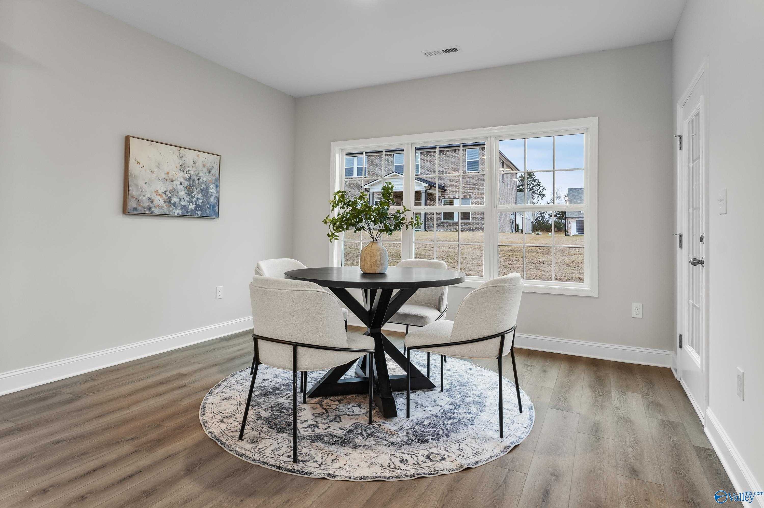 Elegant dining area with round black table, white upholstered chairs, and large windows overlooking yard in Davidson Homes The Finleigh, Toney, Alabama