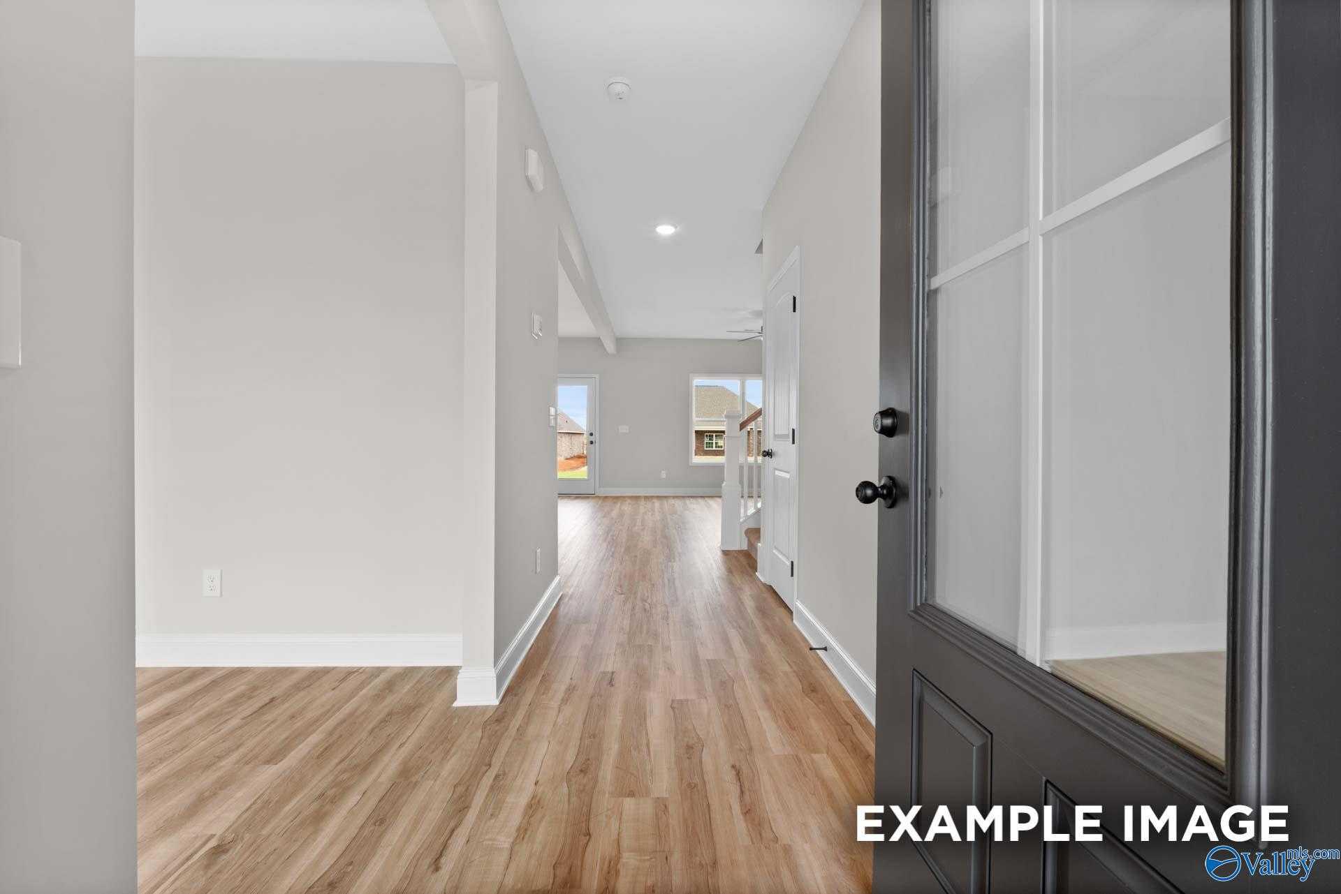 Bright entryway hallway with hardwood floors, neutral walls, and modern glass-front door in The Shelby A home, Athens, Alabama