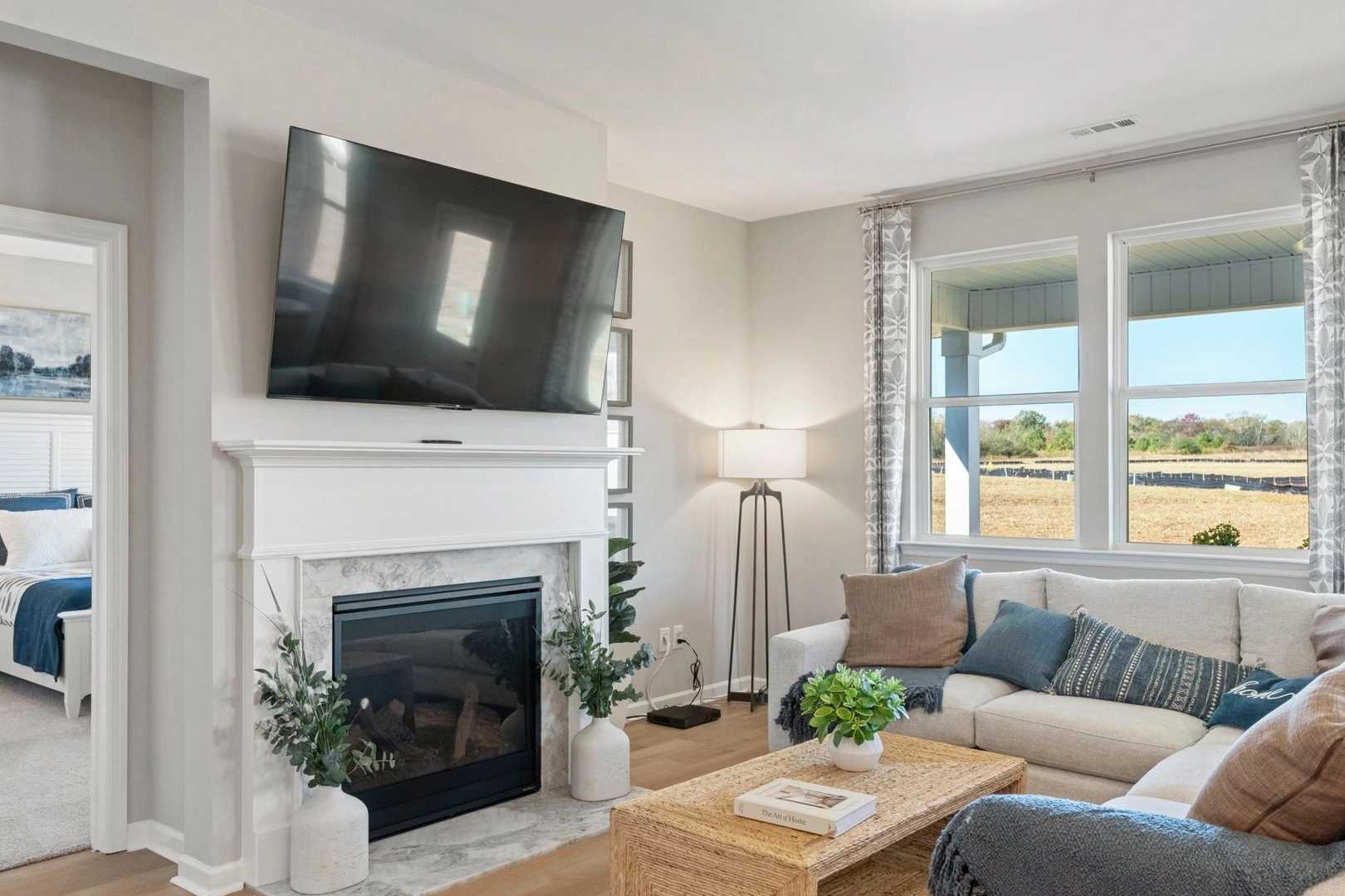Cozy living room at Bailey Park in Fayetteville TN with gas fireplace, mounted TV, beige sofa, plants and scenic field views