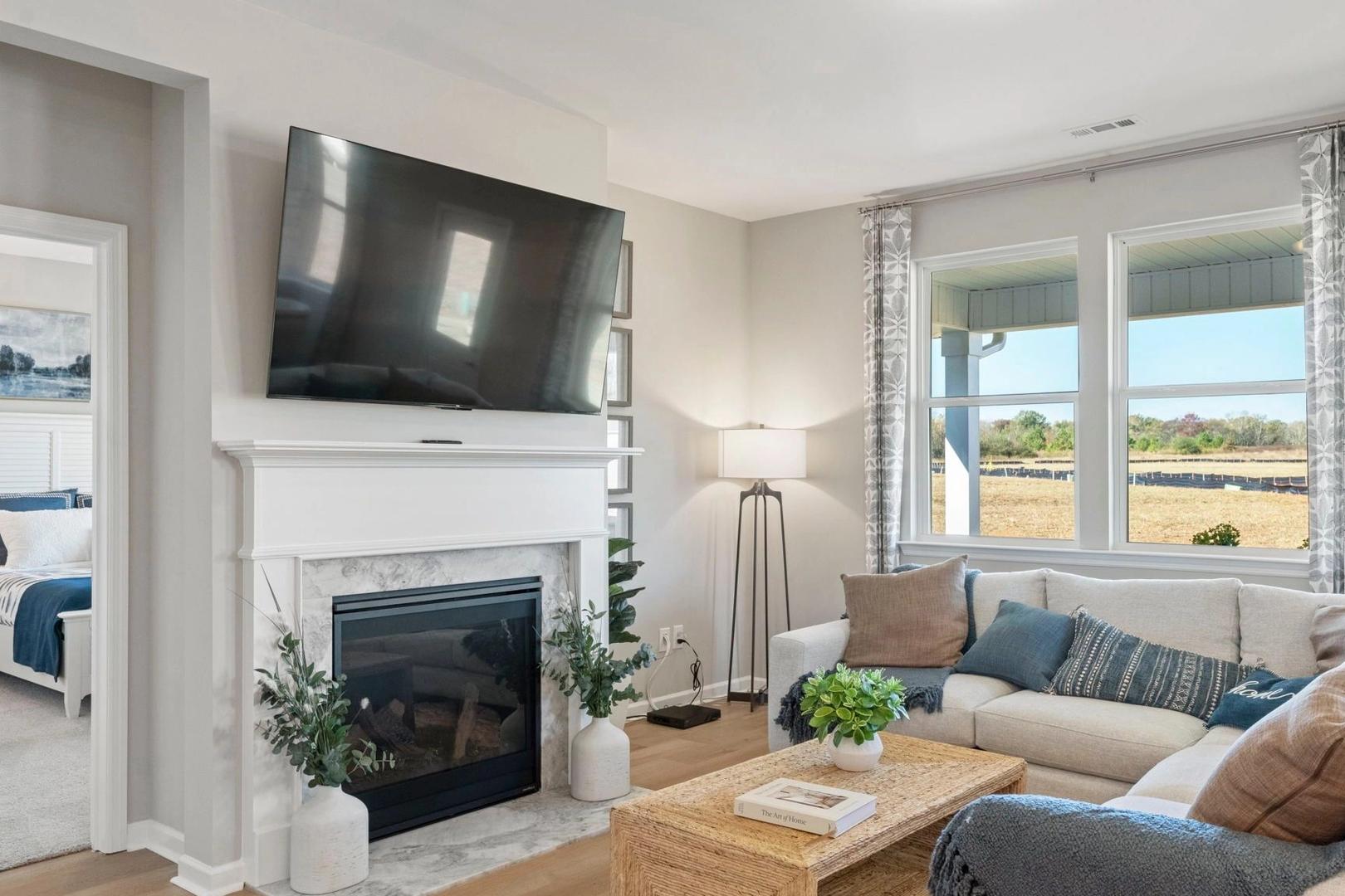 Cozy living room at Bailey Park in Fayetteville TN with gas fireplace, mounted TV, beige sofa, plants and scenic field views