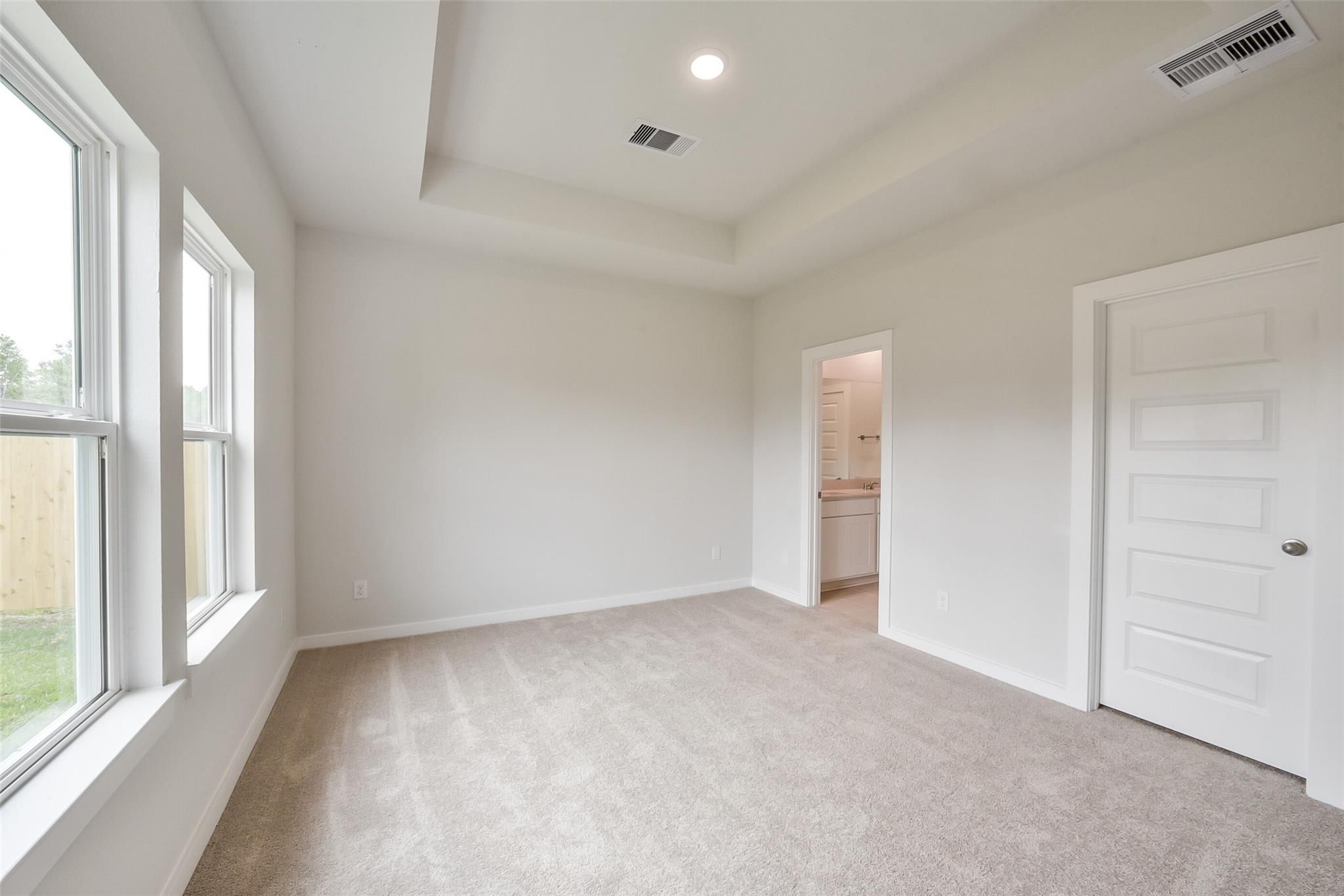 Spacious master bedroom with tray ceiling, large windows, and en-suite bath in Davidson Homes The Frio F, Conroe, Texas