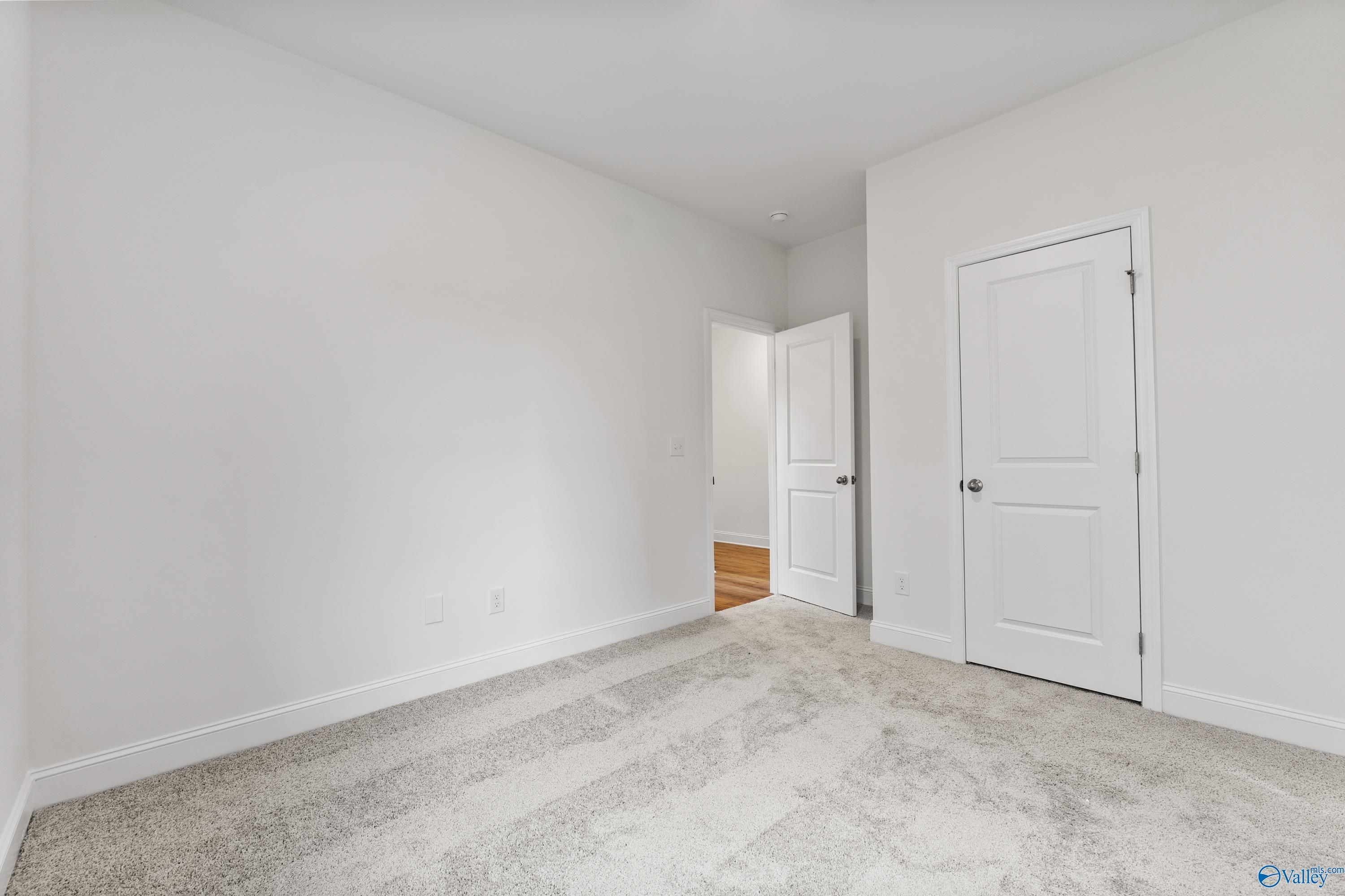 Bright empty bedroom with white walls, light carpet flooring, and double doors in Davidson Homes The Asheville C, New Market, AL