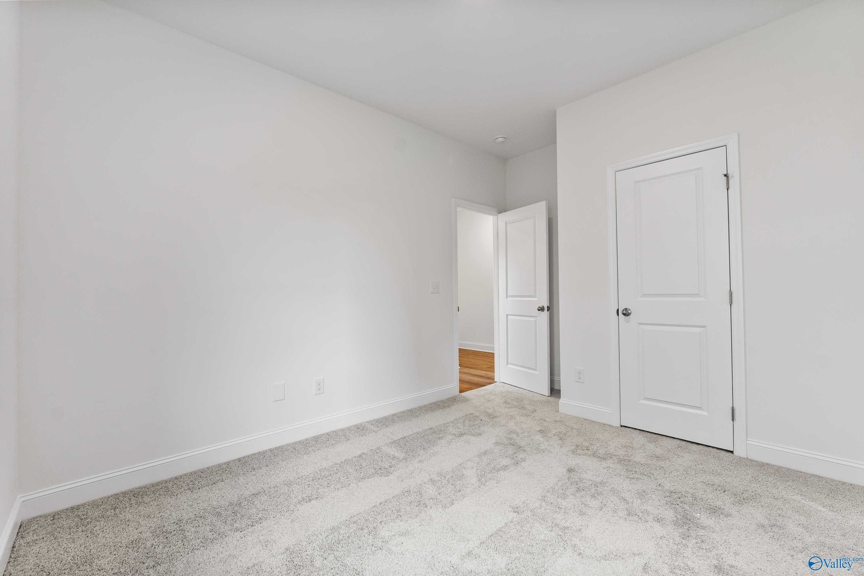 Bright empty bedroom with white walls, light carpet flooring, and double doors in Davidson Homes The Asheville C, New Market, AL