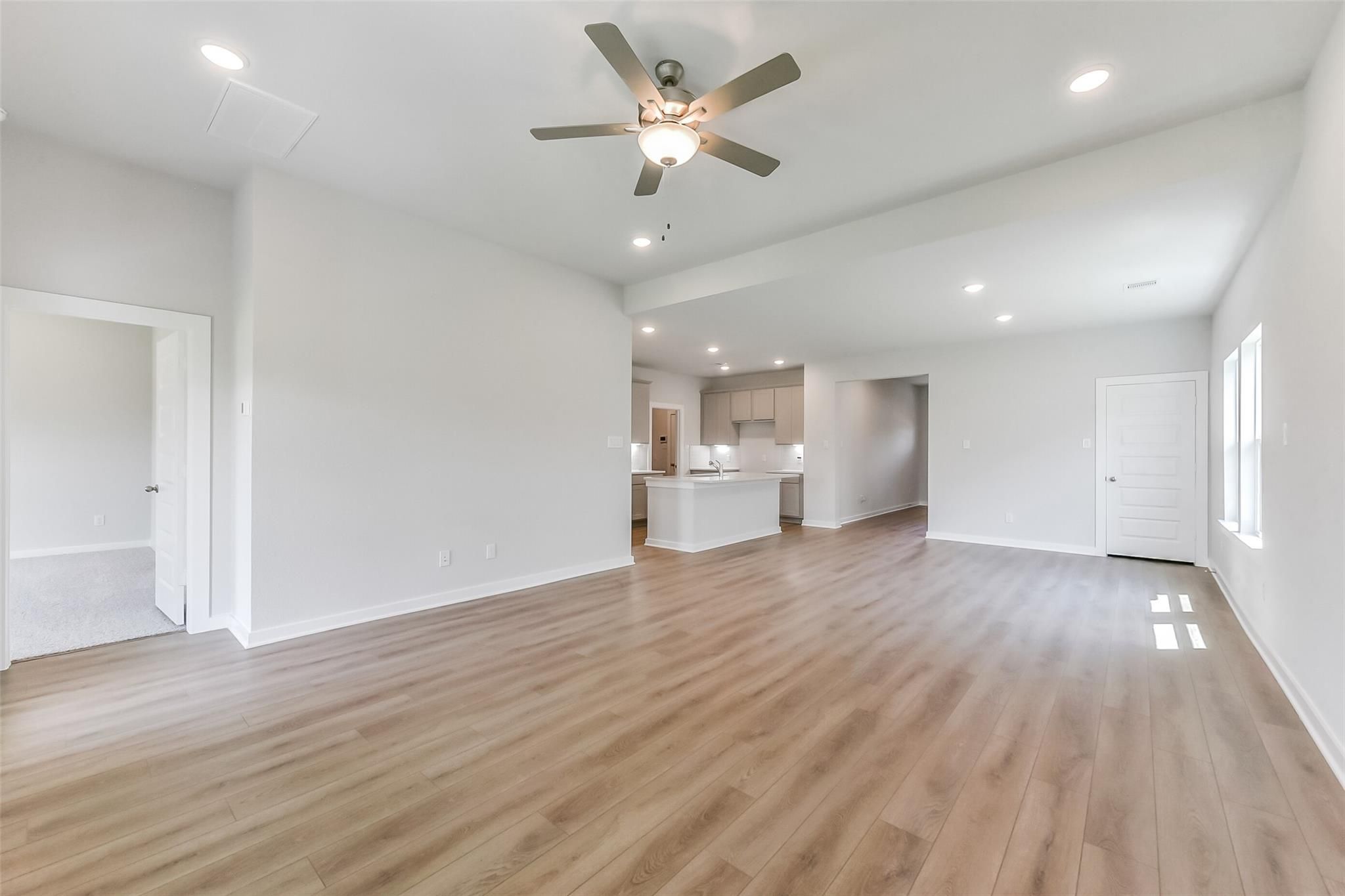 Bright open living room with ceiling fan, laminate wood floors, and adjacent white kitchen island in Davidson Homes The Tierra C, Dayton Texas