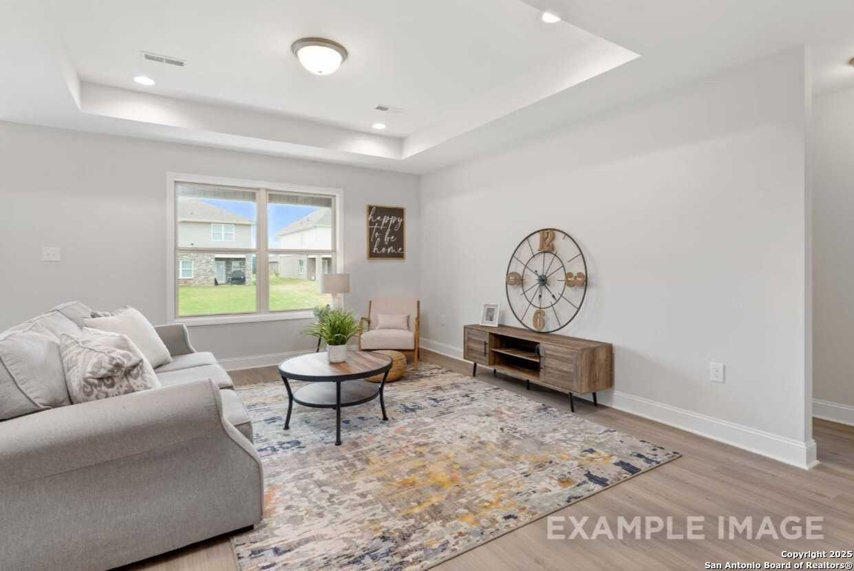 Cozy living room with gray sectional sofa, wooden coffee table, area rug, and backyard window view in Davidson Homes The Asheville K, San Antonio