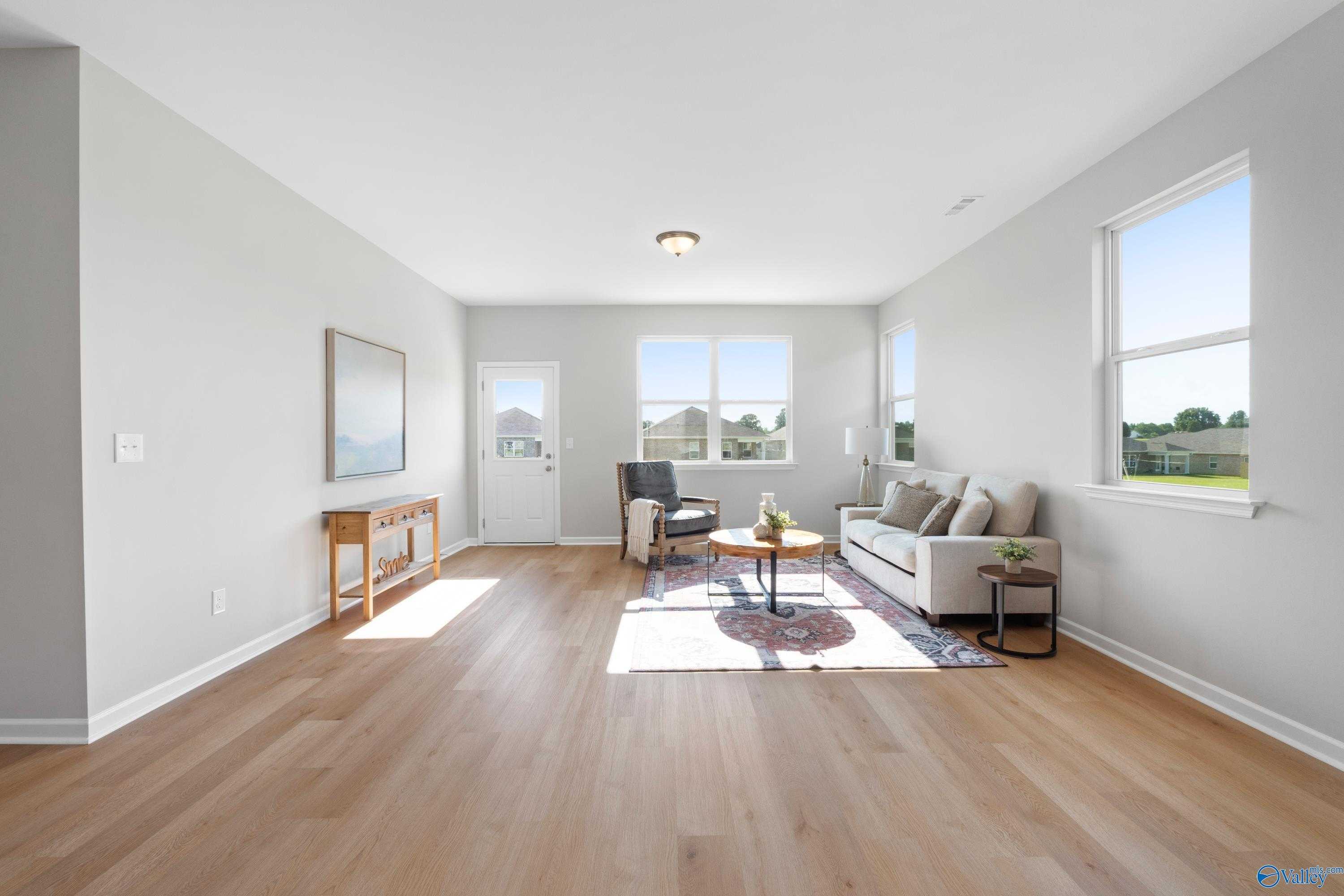 Bright living room with light wood floors, gray walls, sofa, armchair, and large sunny windows in The Aurora 4-bedroom home, Fayetteville, TN