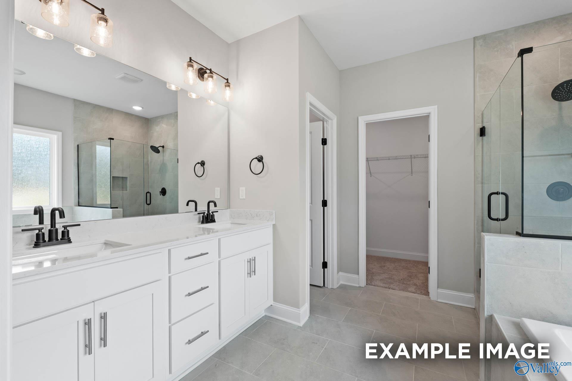 Modern master bathroom with dual vanity, glass-enclosed shower, and walk-in closet in The Montgomery B, Decatur, Alabama.