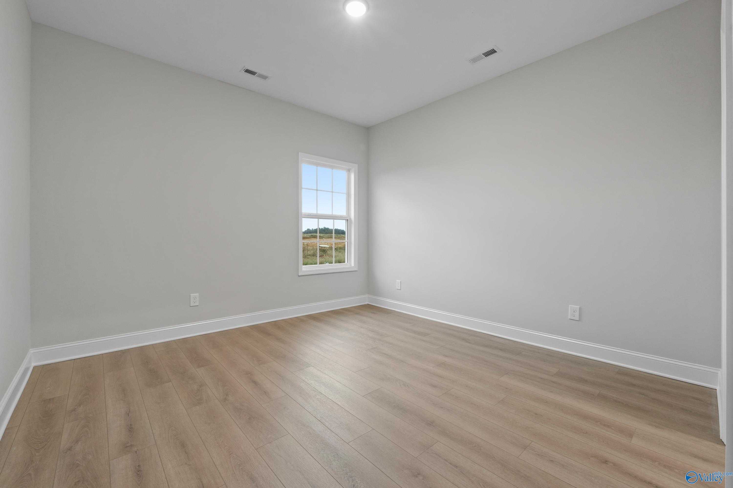 Bright empty bedroom with light gray walls, large window, and laminate wood flooring in Davidson Homes The Lanier, Harvest AL