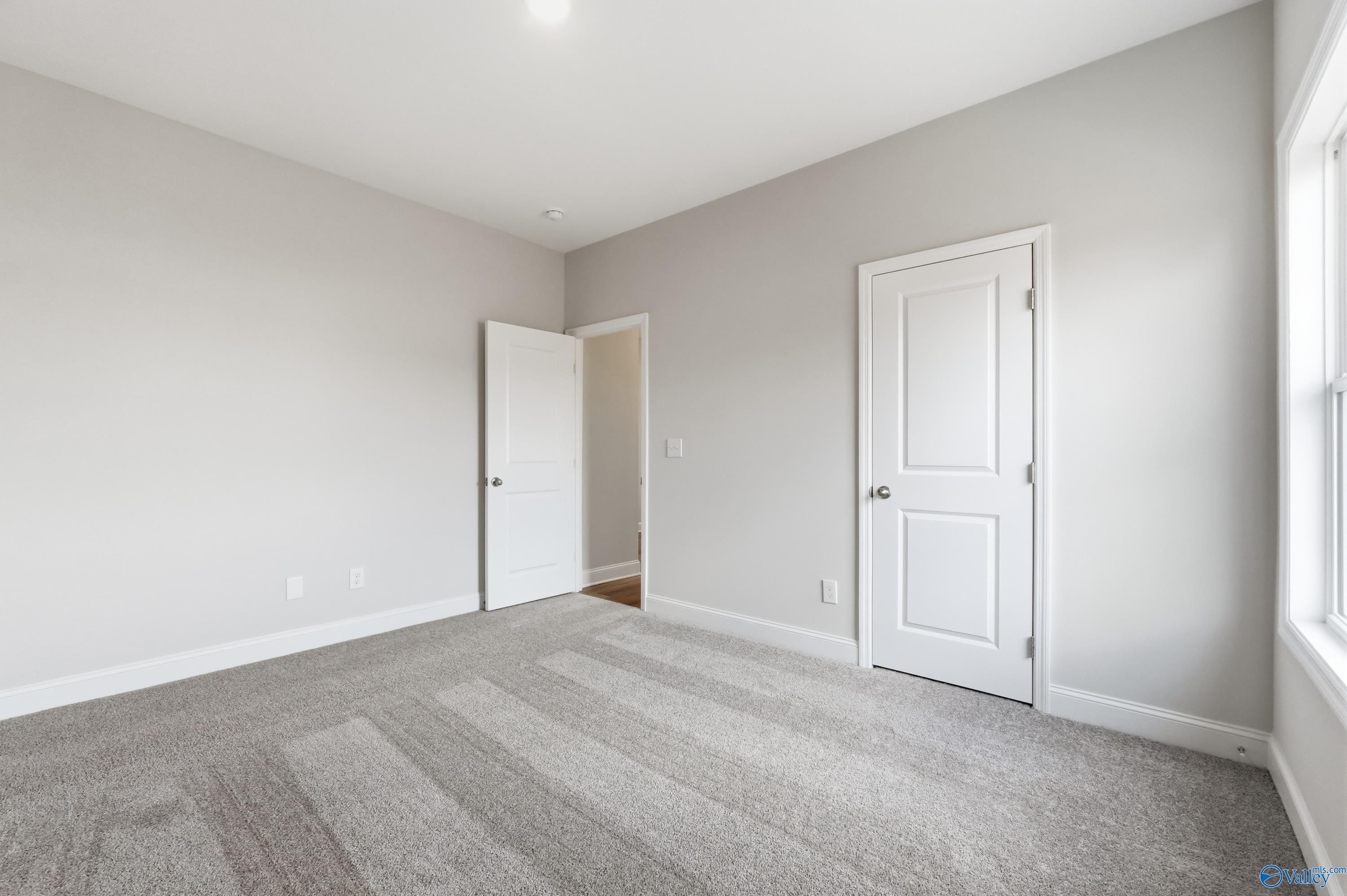 Empty bedroom with light gray walls, white doors, and plush gray carpet in 4-bedroom Davidson Homes The Daphne C, Toney, Alabama